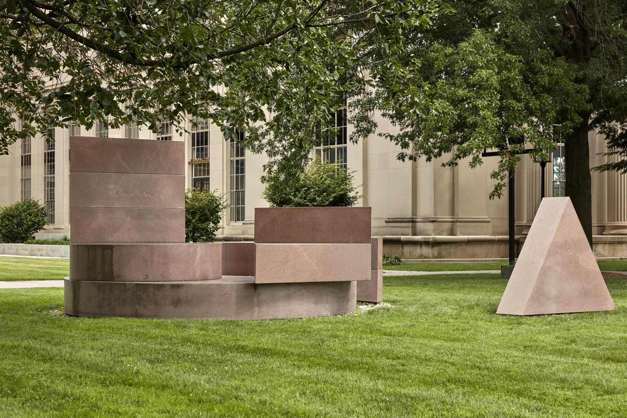 Pink Laurentian granite sculpture featuring geometric shapes on a lawn.