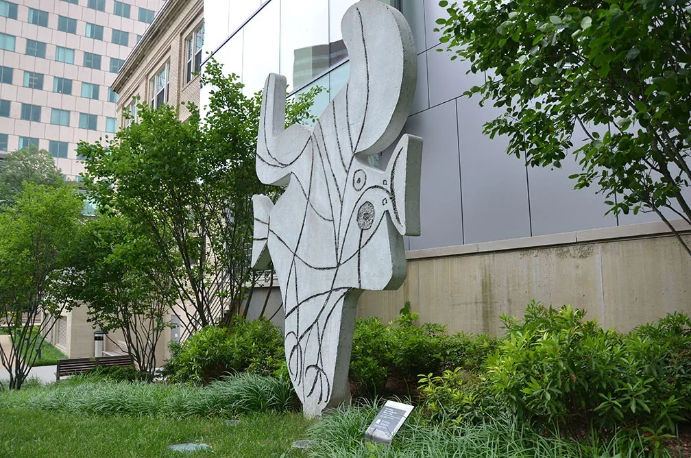 Concrete cut-out sculpture representing a bird with head and beak to the right, tail to the left, feet below, and spread wings above