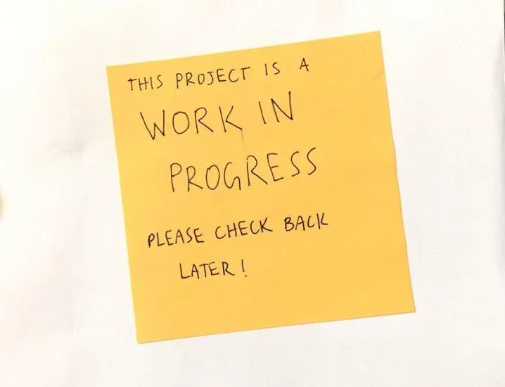 White postcard with a yellow sticky note that reads "this project is a work in progress please check back later!