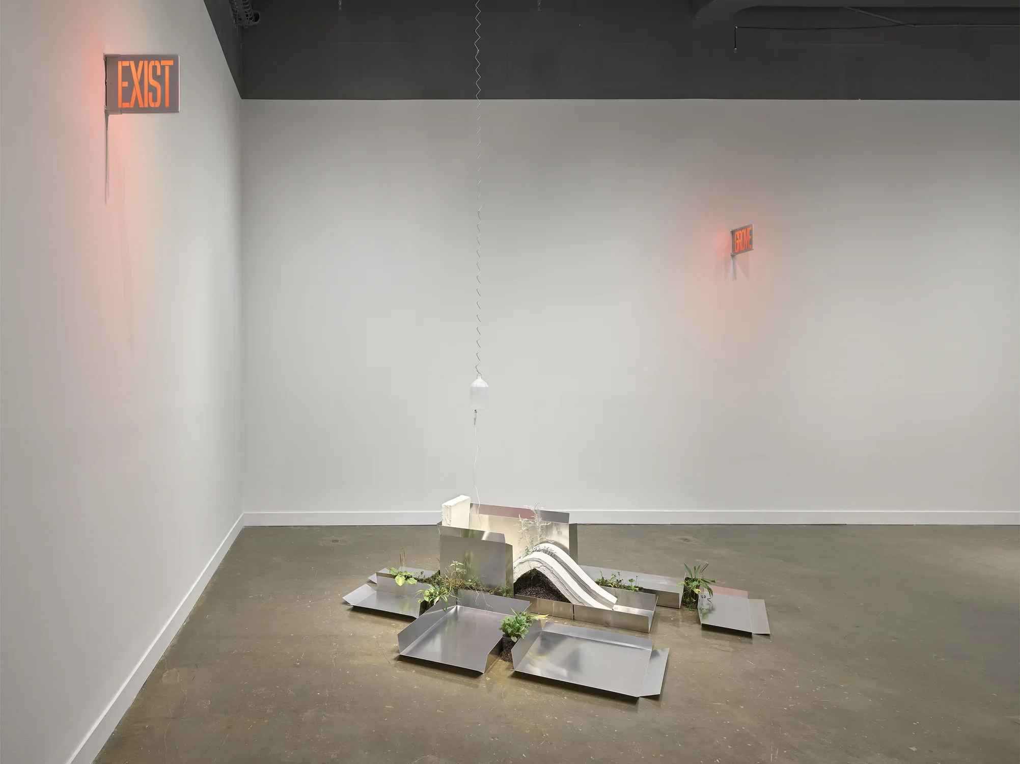 A gallery at the MIT List Visual Arts Center features sculptures consisting of white plaster slumps, aluminum sheets, weeds, and red glowing signs on the walls.