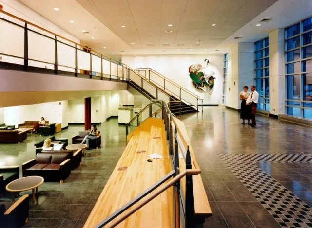 Image of a long room with a lounge area on the lower left are and a hall with a tiled floor on the right.