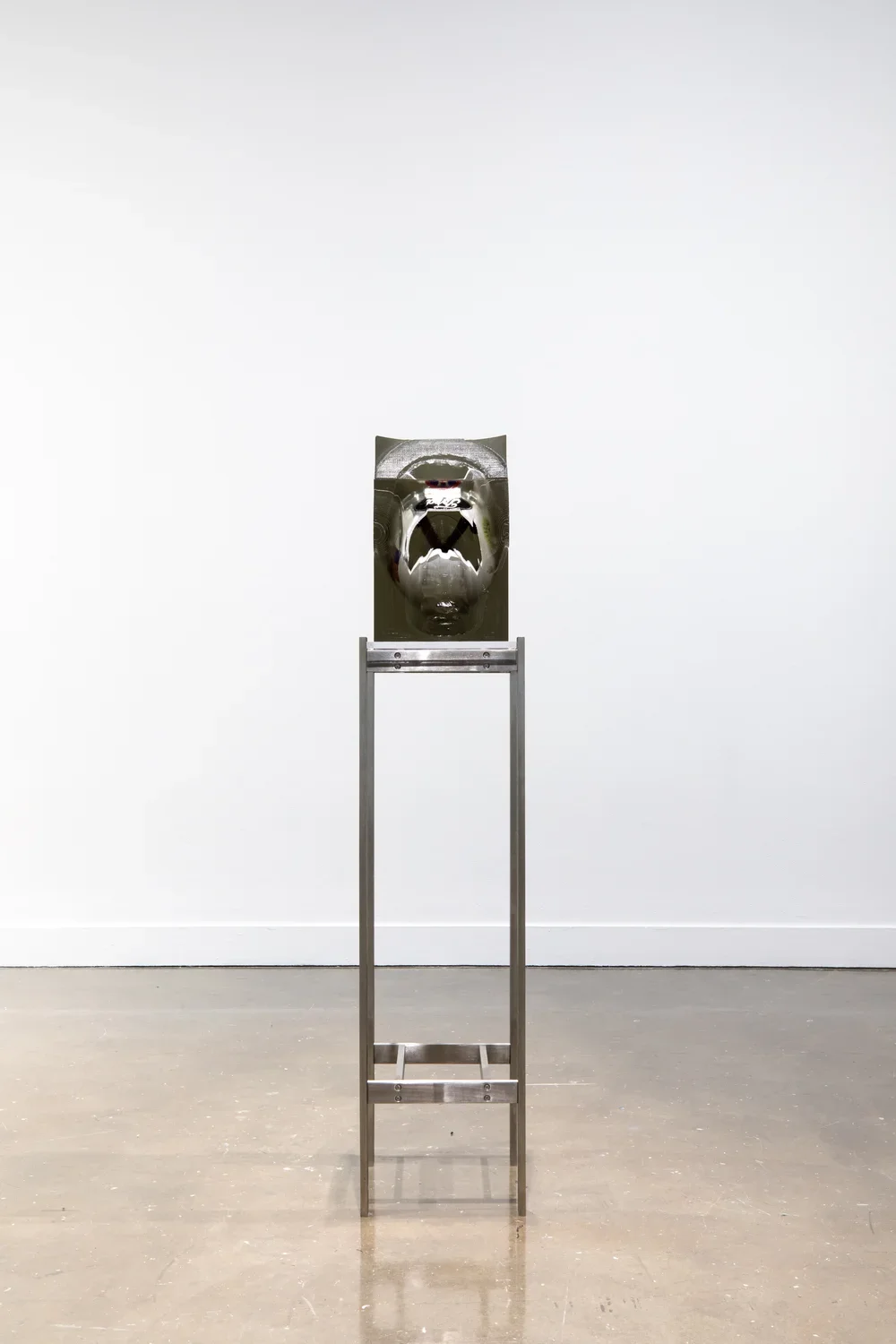 Installation view of a white and black helmet encased in a rectangular block of resin on a tall metal stand. 