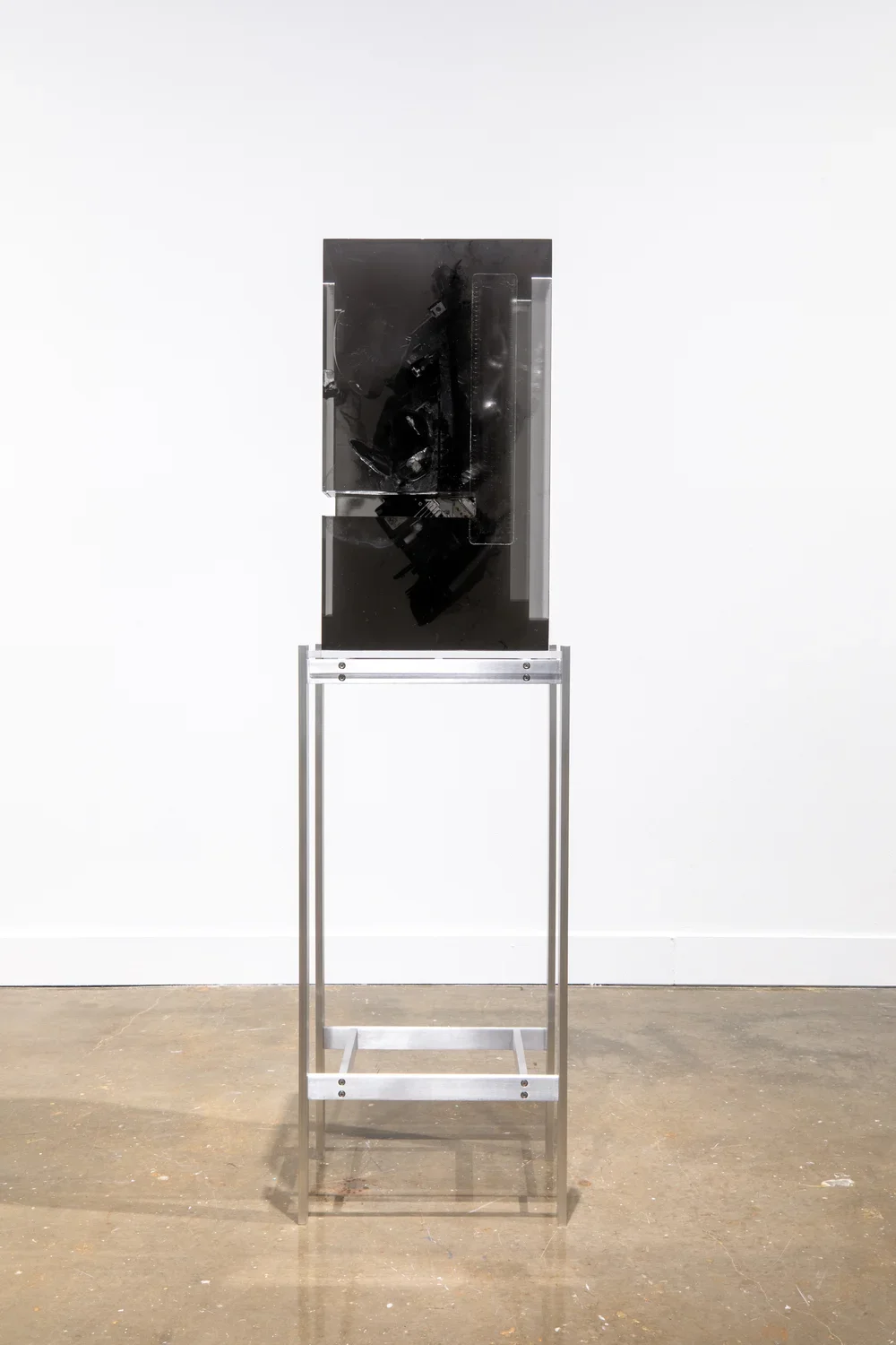 Installation view of a black headlight encased in a block of dark resin on a tall metal stand. 