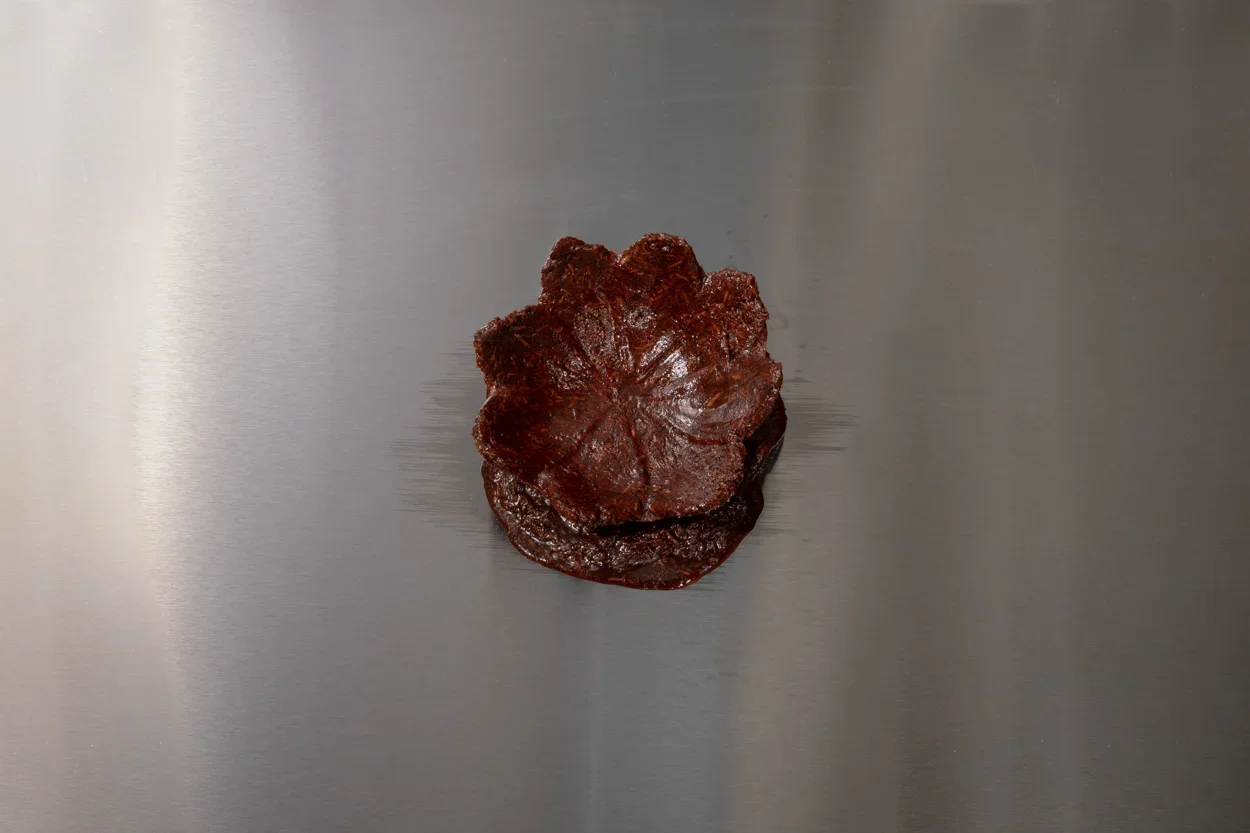 View from above of a deep red bukhoor incense cast in the shape of a water lily on a silver steel table. 