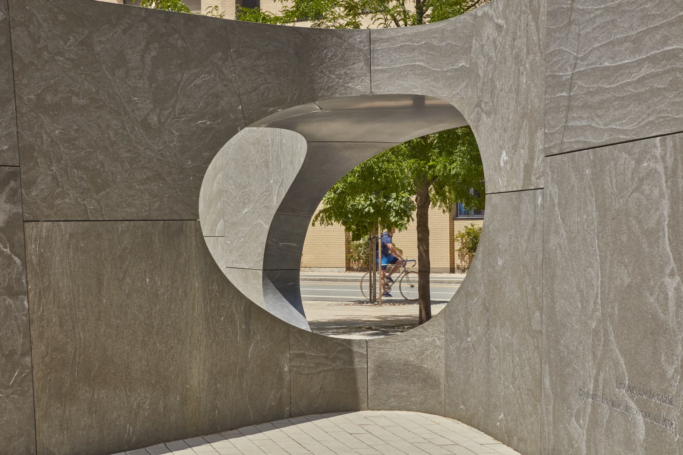 Close up of a large granite sculpture with a rectangular shape that has an oval cut out in the center that peaks through to the main rood next to the sculpture. 