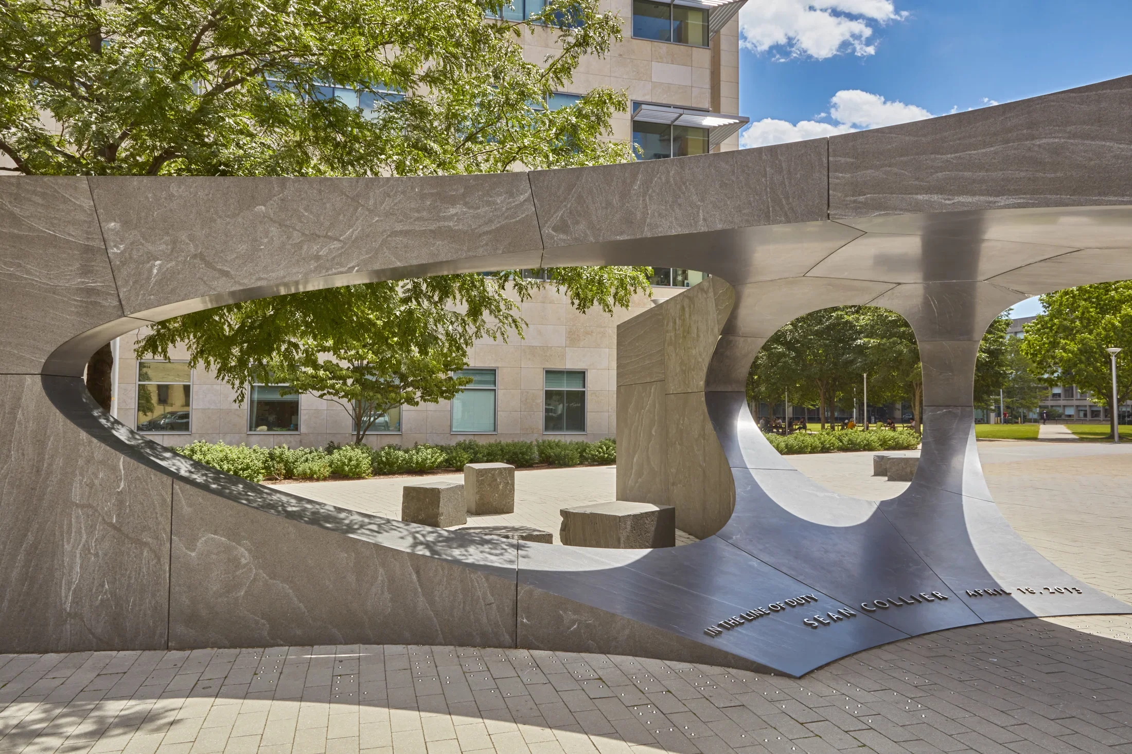 Close up of a large granite sculpture with a rectangular shapes that have oval cut outs in the center that peaks through to the main rood next to the sculpture. 