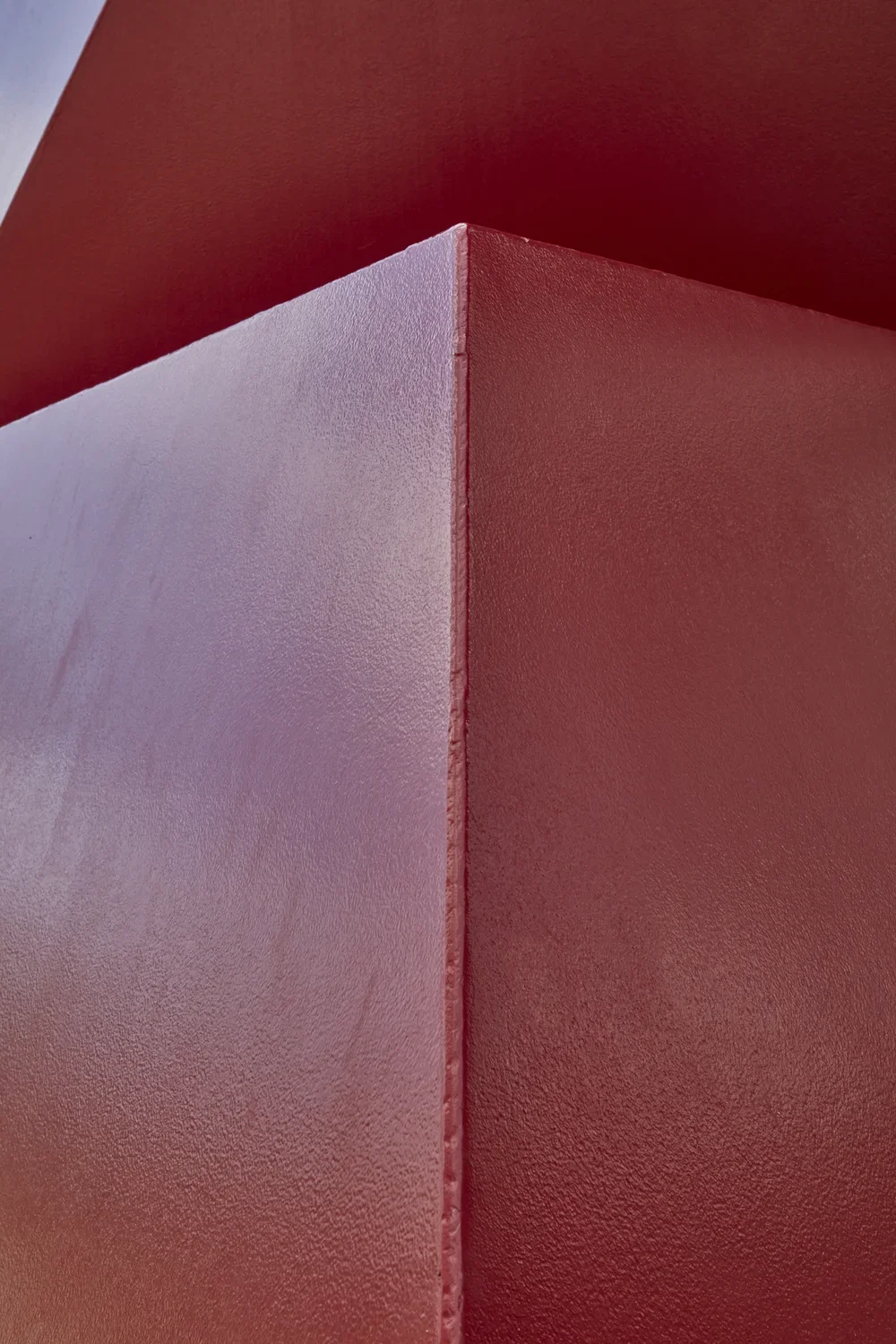 Detailed view of a red painted steel sculpture with a smooth surface and hard edges. 
