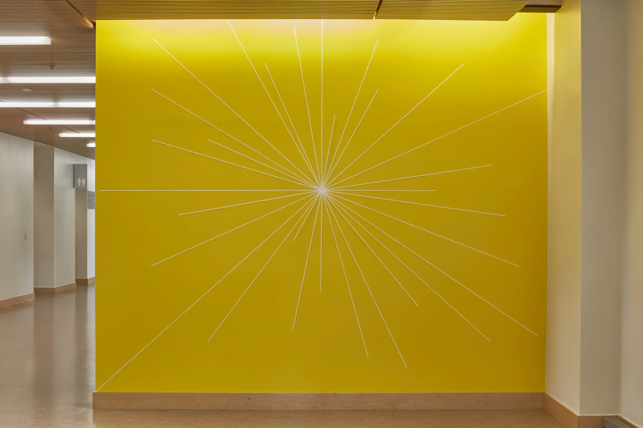 Bright yellow wall with a drawing featuring thin lines that come out from the center of the wall to form a sun like shape. 
