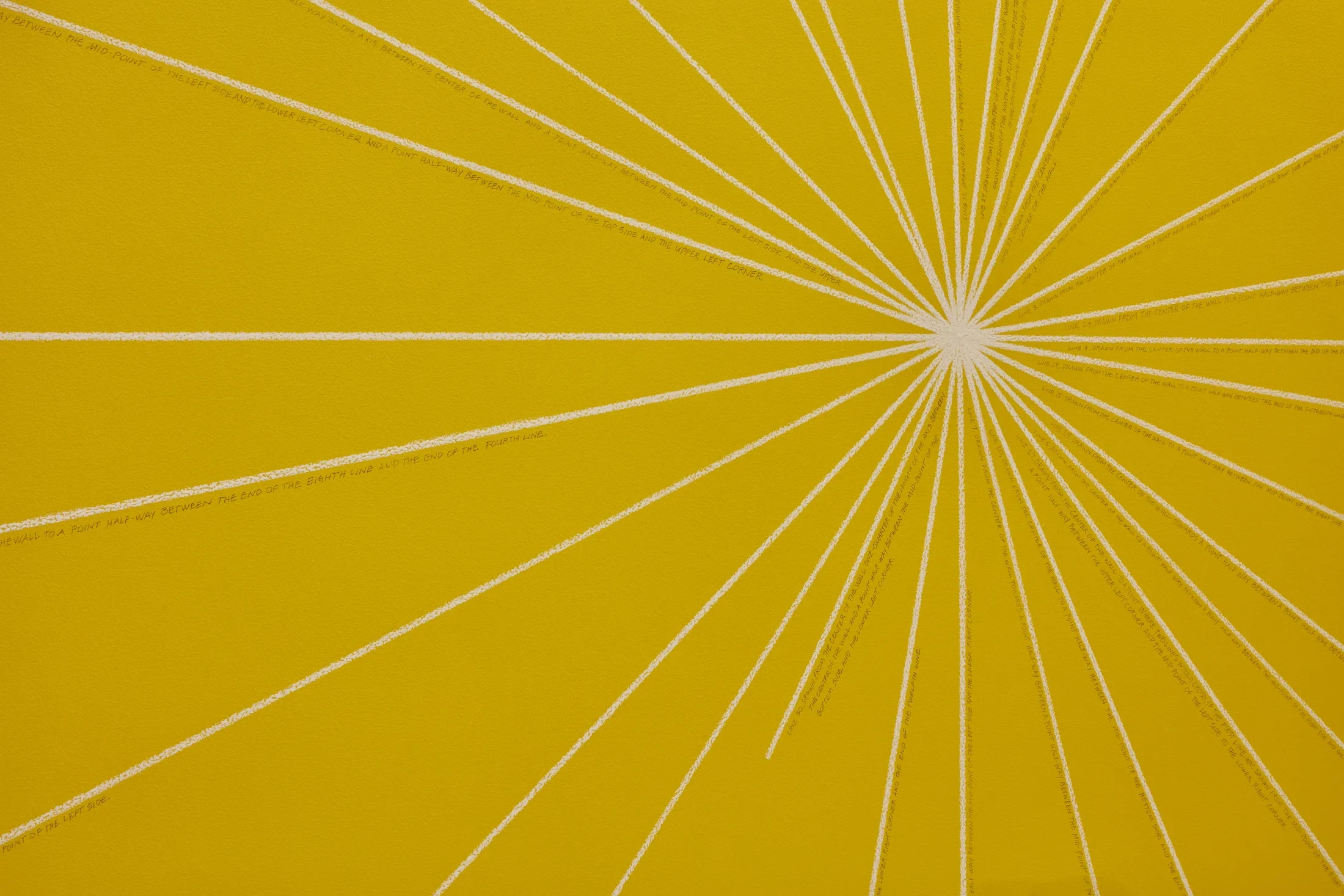Bright yellow wall with a drawing featuring thin lines that come out from the center of the wall to form a sun like shape. 