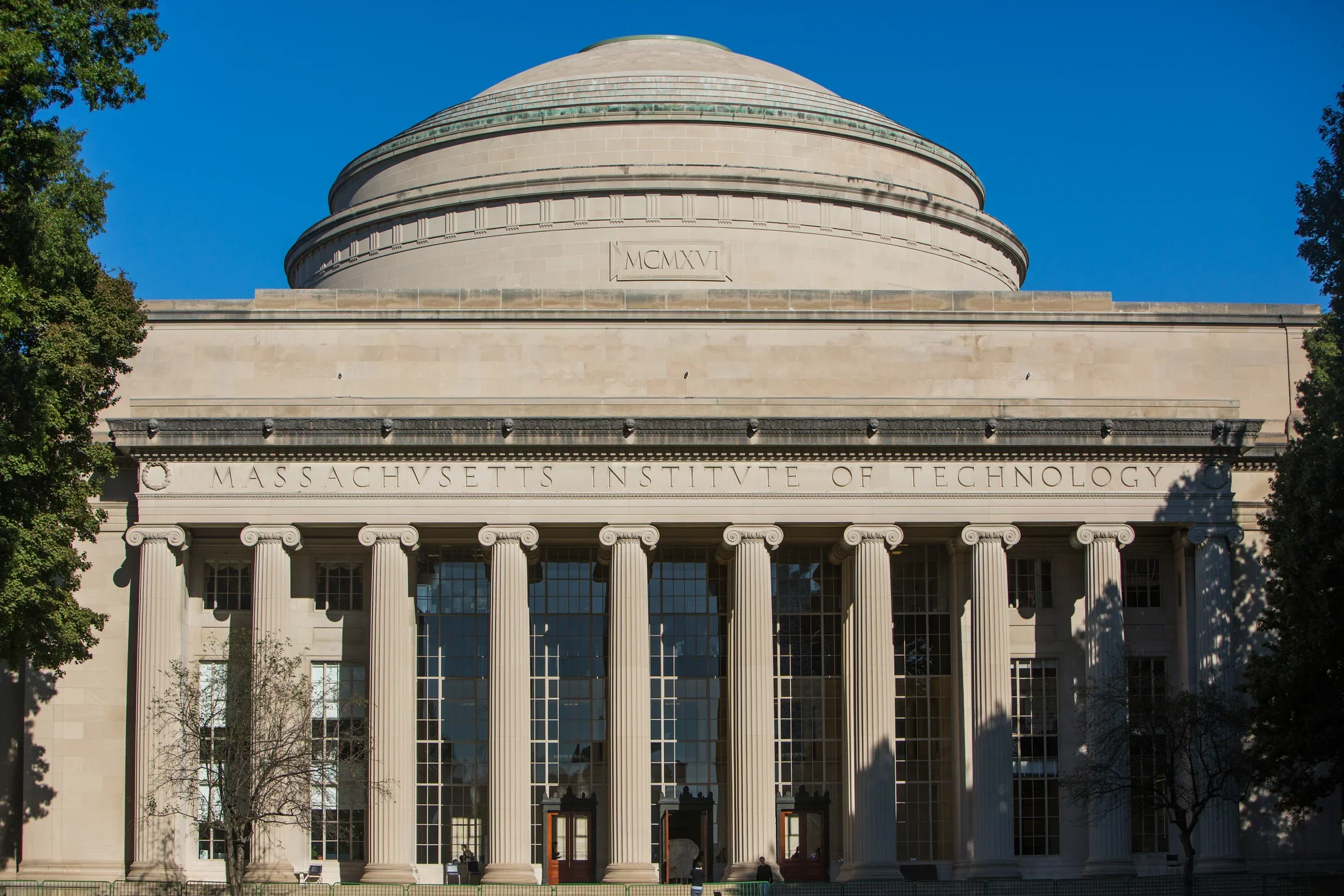 Domed stone building with tall columns against a blue sky and trees peaking out on the left and right. 
