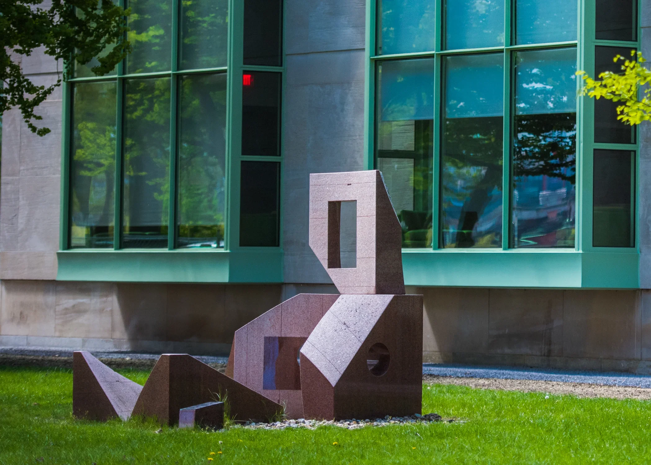 Granite sculpture resembling a man with a tv on his head and a brick building with large glass windows behind. 