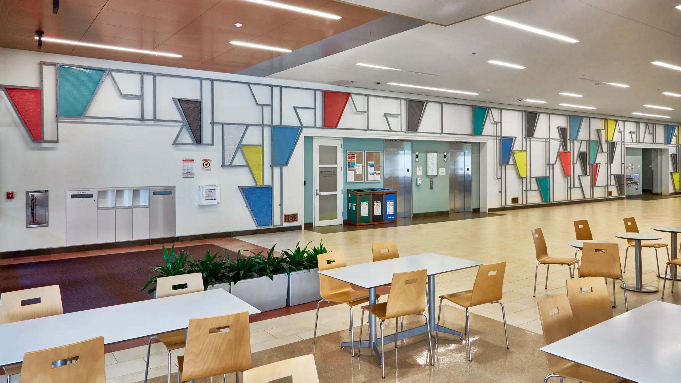 Painted steel sculpture on a wall featuring triangular shapes and lines and tables and chairs in the foreground. 