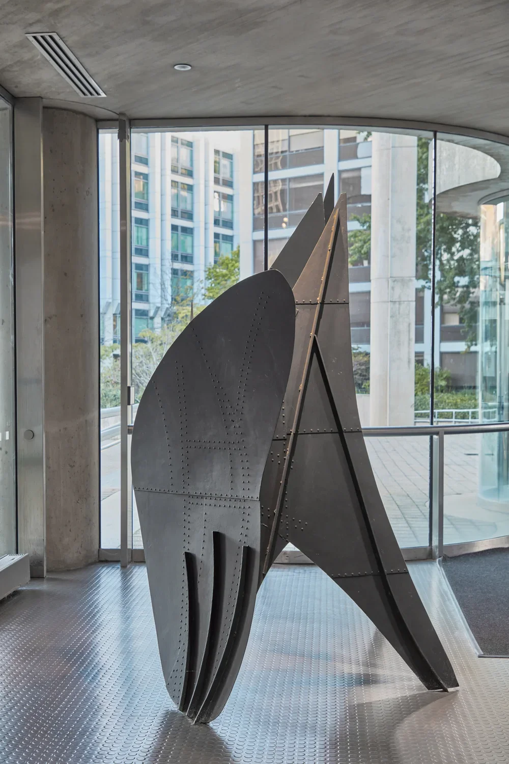 A downsized model of a black steel sculpture with three points of contact on the ground and rounded edges at the top. 