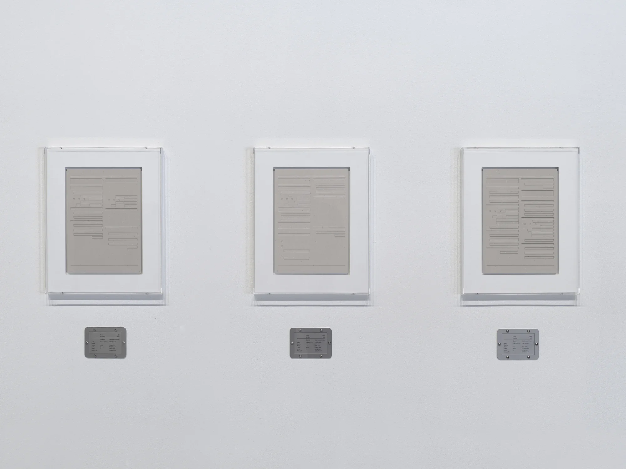 Three rectangular plaster works in white frames are hung side-by-side, each with a horizontal steel plaque below.