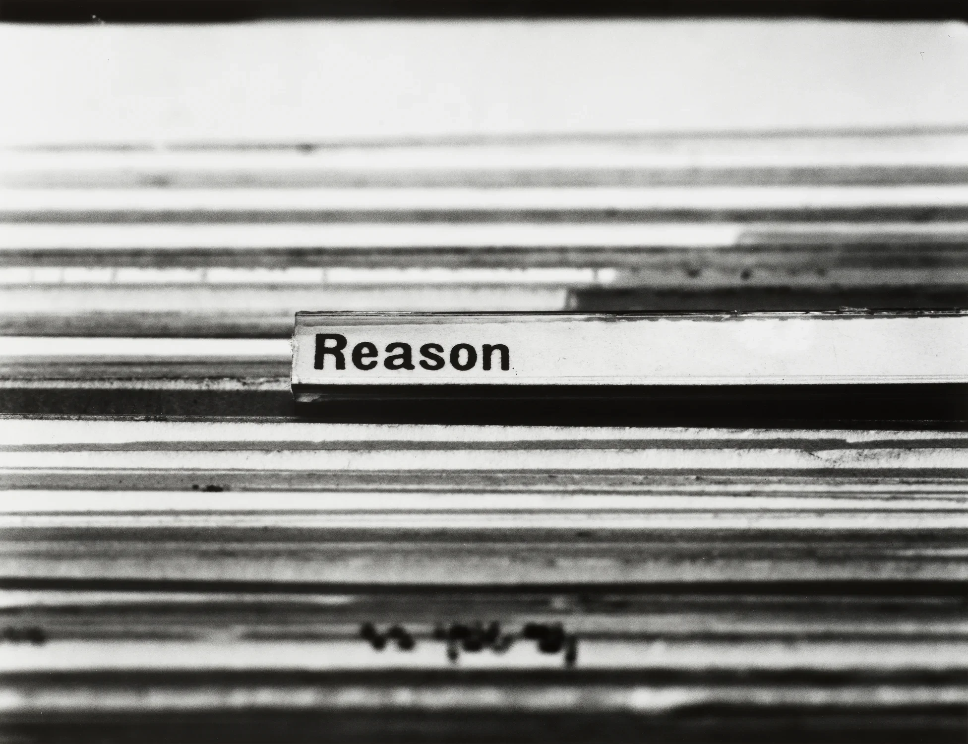 Black and white detail image of many file folders in a row. There is one label tab highlighted with black bolded text. The text reads "Reason"