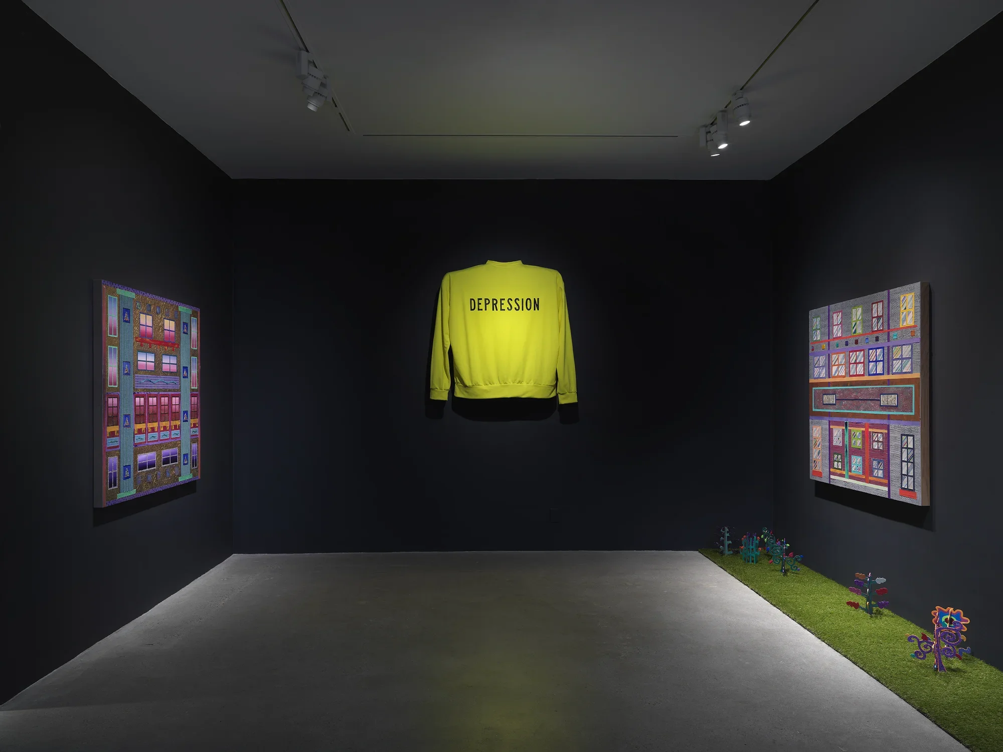 An art gallery with dim lighting showcases three artworks on the walls. In the‬ ‭ center, a bright neon yellow sweater with the word ‘Depression’ written across it is‬ ‭ displayed, elevated off the wall. On the left and right walls, two paintings with bright‬ ‭ geometric forms hang across from one another. A strip of astroturf on the floor lines the‬ ‭ right wall with small painted wooden plants emerging from it.‬