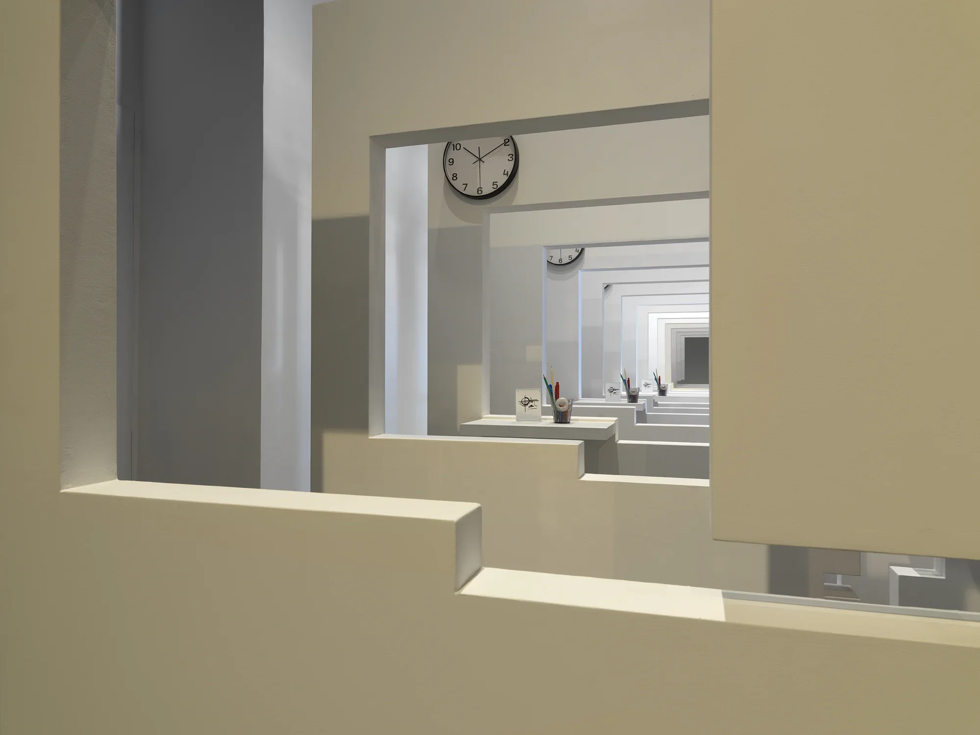 A series of white walls with a window cutout that has a view of the next white wall with a window cutout. There is a cup with office supplies on the window ledge of each wall.