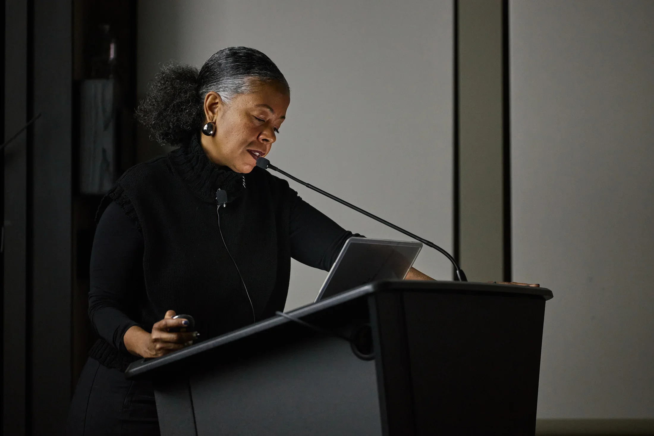 A woman is standing in a dimly lit room, behind a podium, and speaking into a microphone.
