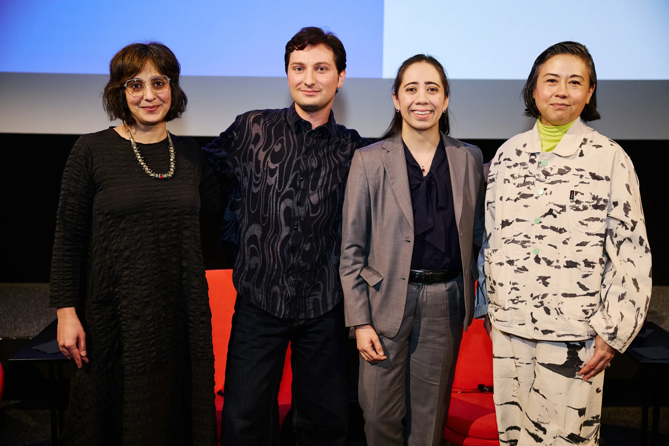 A group of four people standing in a row on stage in front of a projector screen.