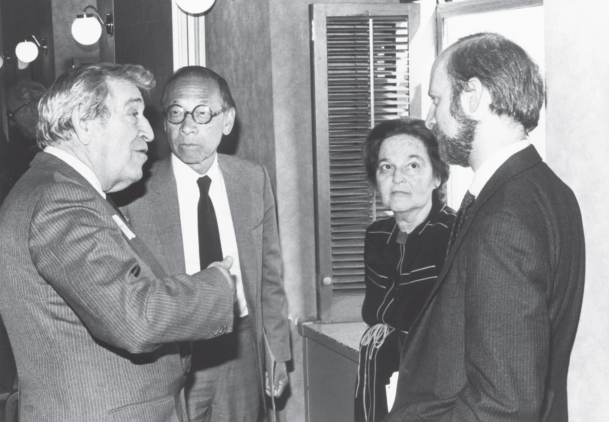 Black and white photograph of four people in conversation standing in a circle.