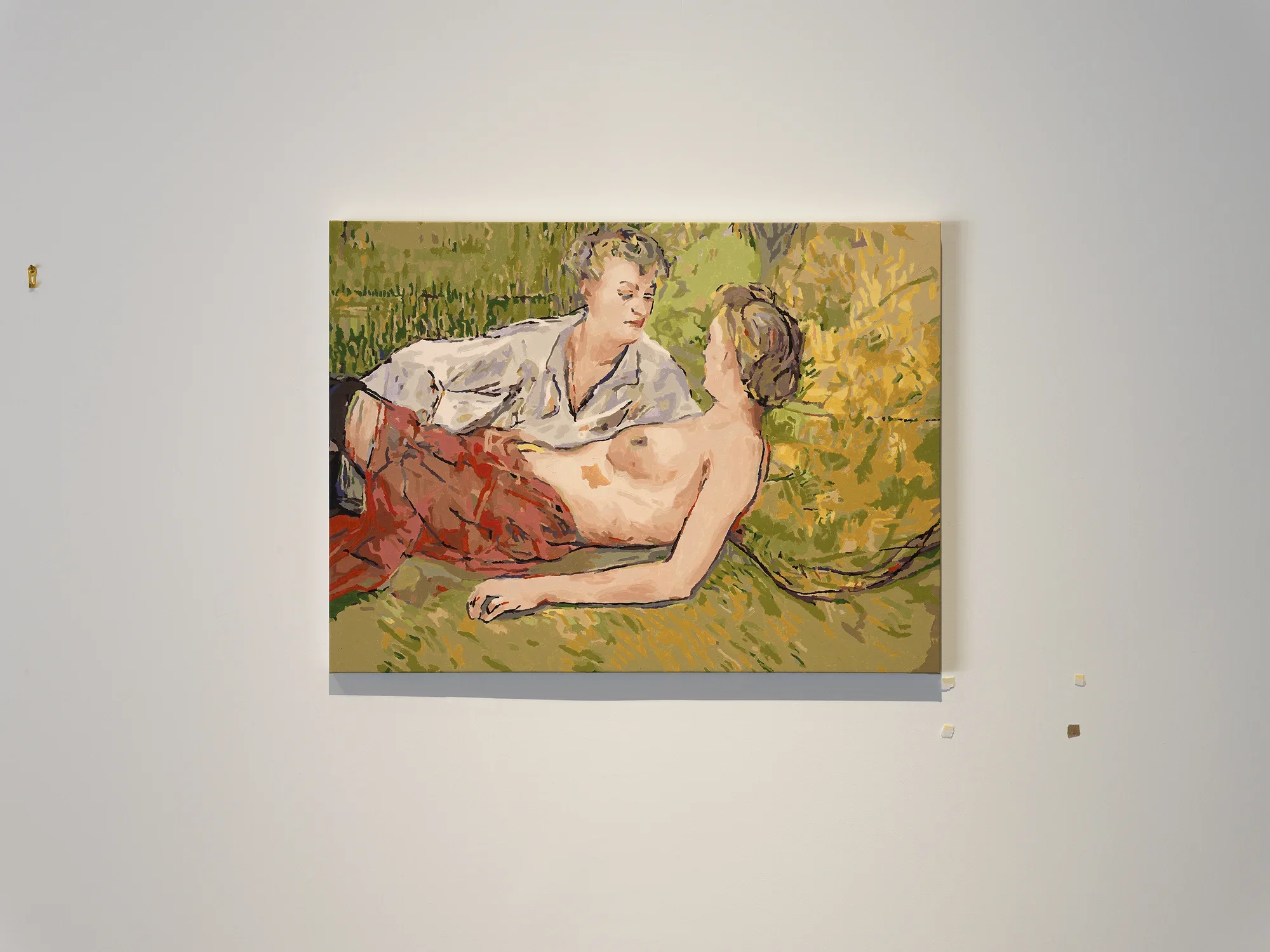 A golden-green painting in a 19th-century European style shows two women half-reclining: The one in the foreground is topless, and seems almost cradled by her clothed companion, who leans over her. The painting is crude and seems separated into layers of uniformly applied color.  The white wall around the painting is marked by golden hanging hardware and irregular square of tape-like material.