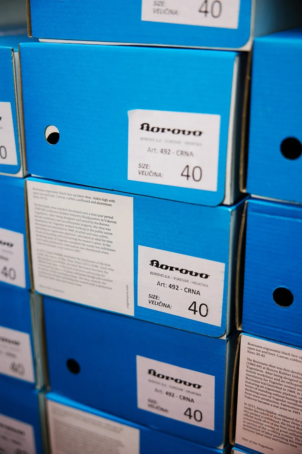 A stack of blue shoe boxes fills the entirety of the frame: each is labeled with a Borovo logo, a numerical size, and an explanatory label of a couple paragraphs.