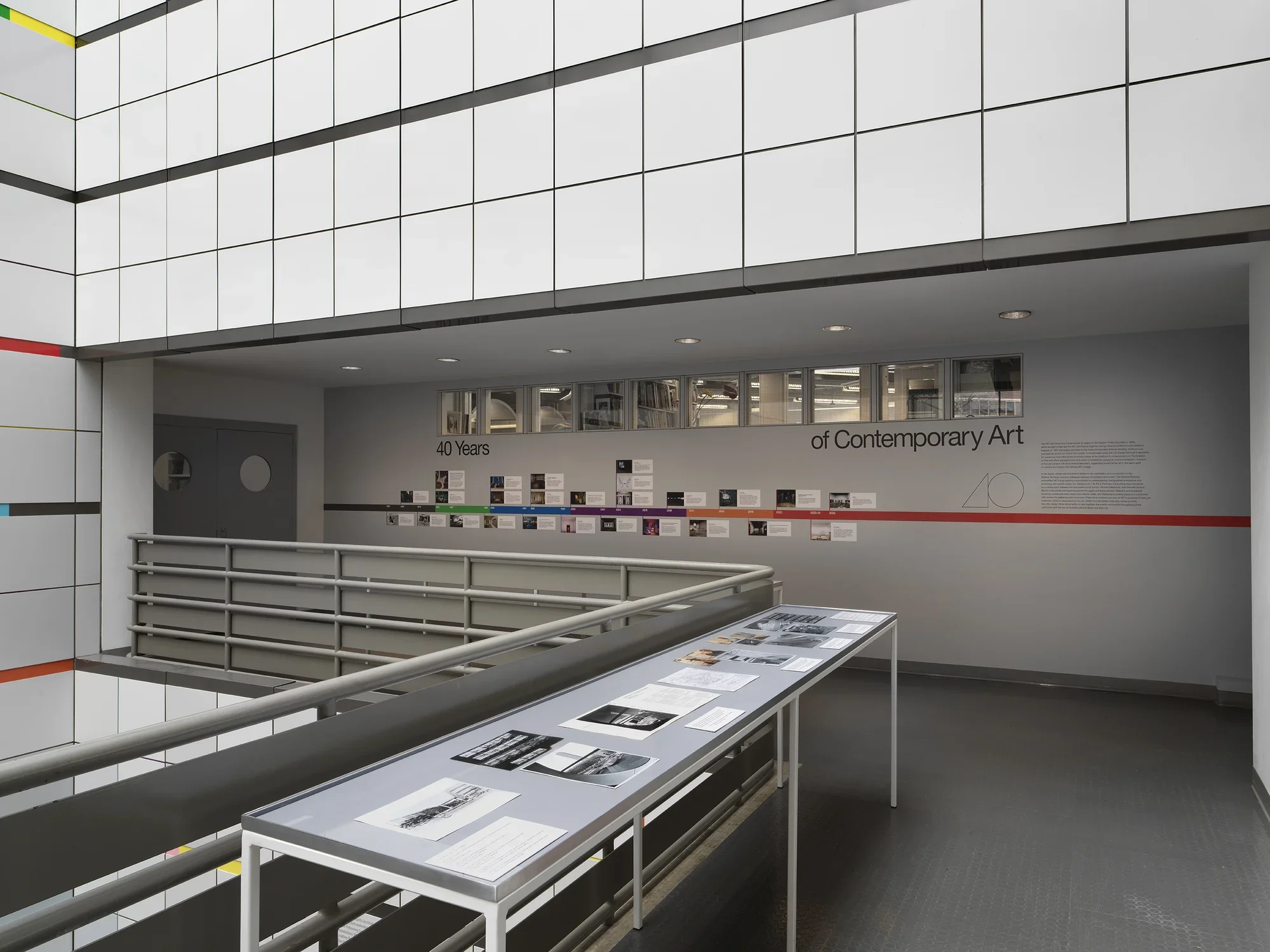 A large vitrine encasing black and white photos in the middle of an open atrium. A colorful timeline with images is adhered on the wall behind.