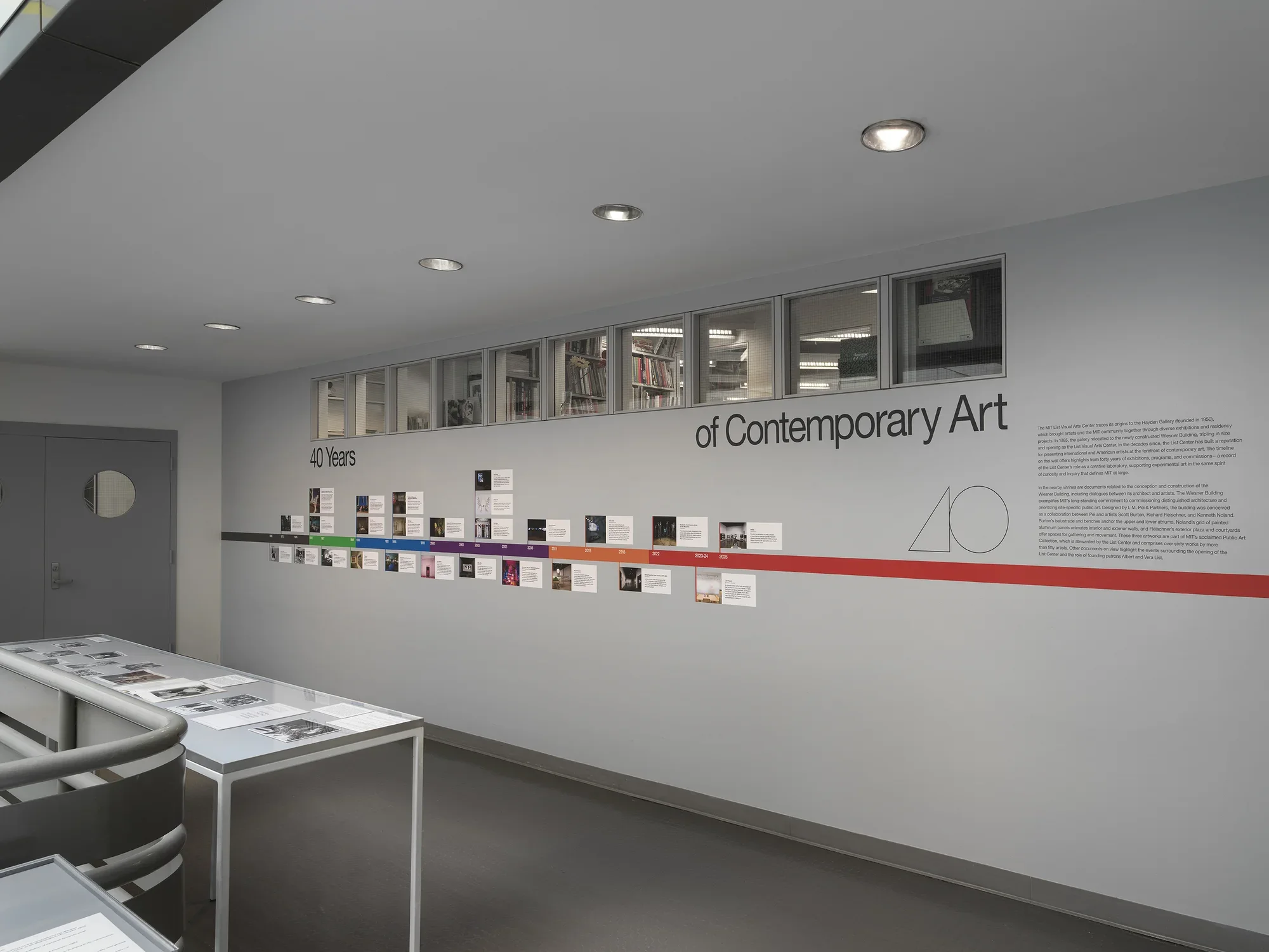 A large vitrine encasing black and white photos in the middle of an open atrium. A colorful timeline with images is adhered on the wall behind.