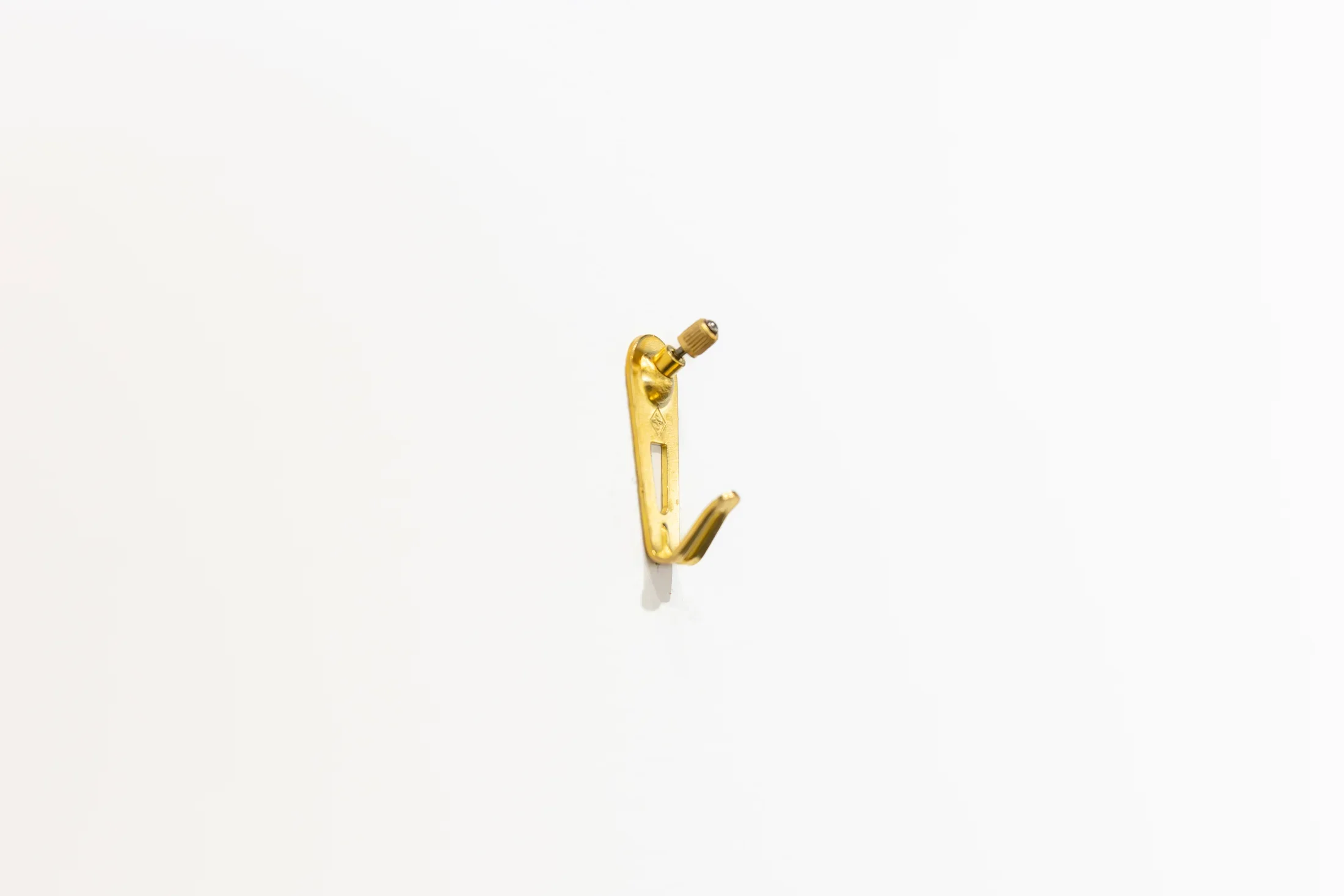 A single brass picture hook is mounted on a white wall.