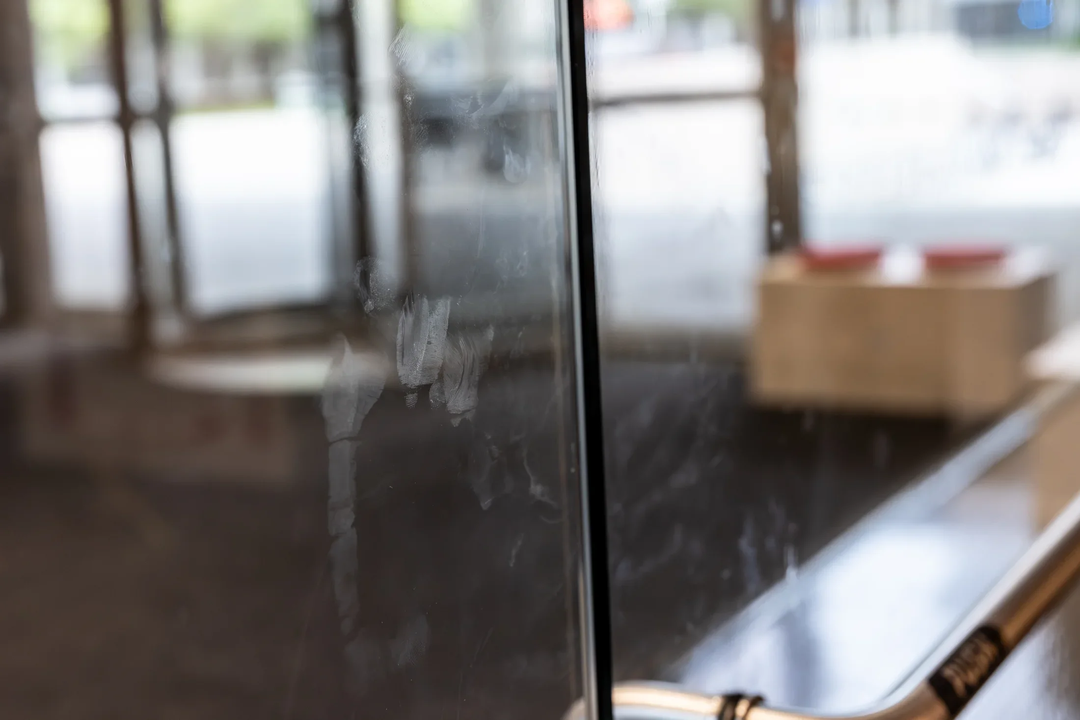 A close-up of a glass door covered in many white smudges and fingerprints. A silver handle with the word 'PUSH' is visible in the lower right, and a blurry interior is seen through the glass.