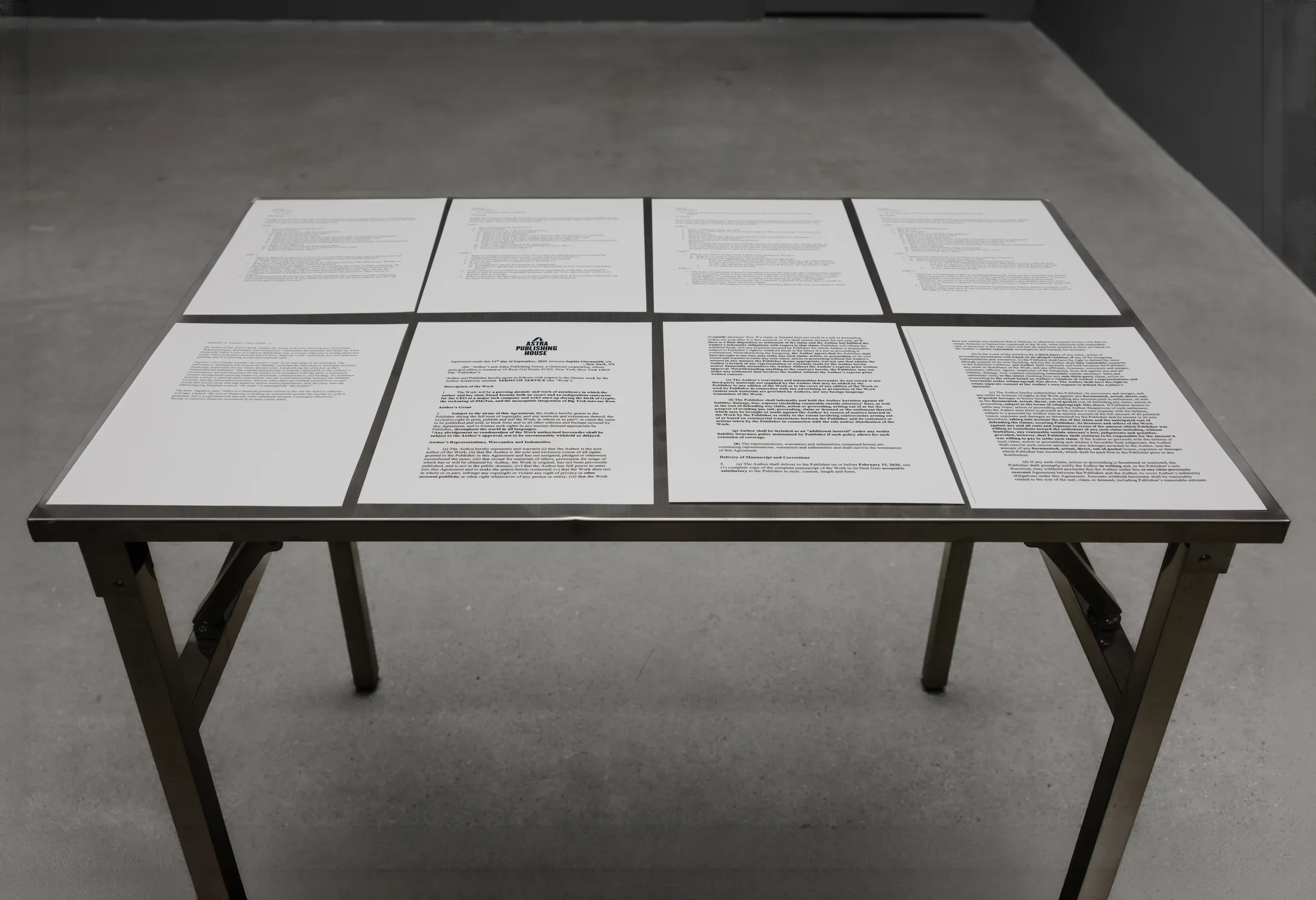 Eight pieces of letter-sized paper lie in a grid, edges nearly touching, across the entirety of the surface of a metal table. The pages are filled with printed text. One of the pages closer to the camera features a logo at the top reading “Astra Publishing House.”