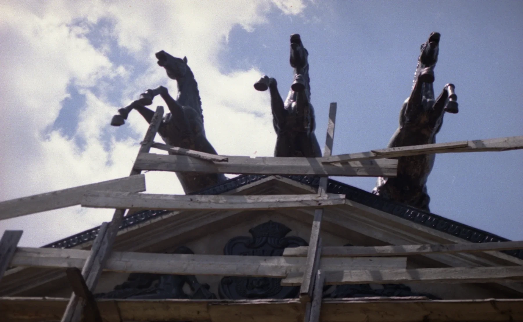 Video still showing a building rooftop adorned with three sculptural horses hanging off the front as if they are mid-gallop.