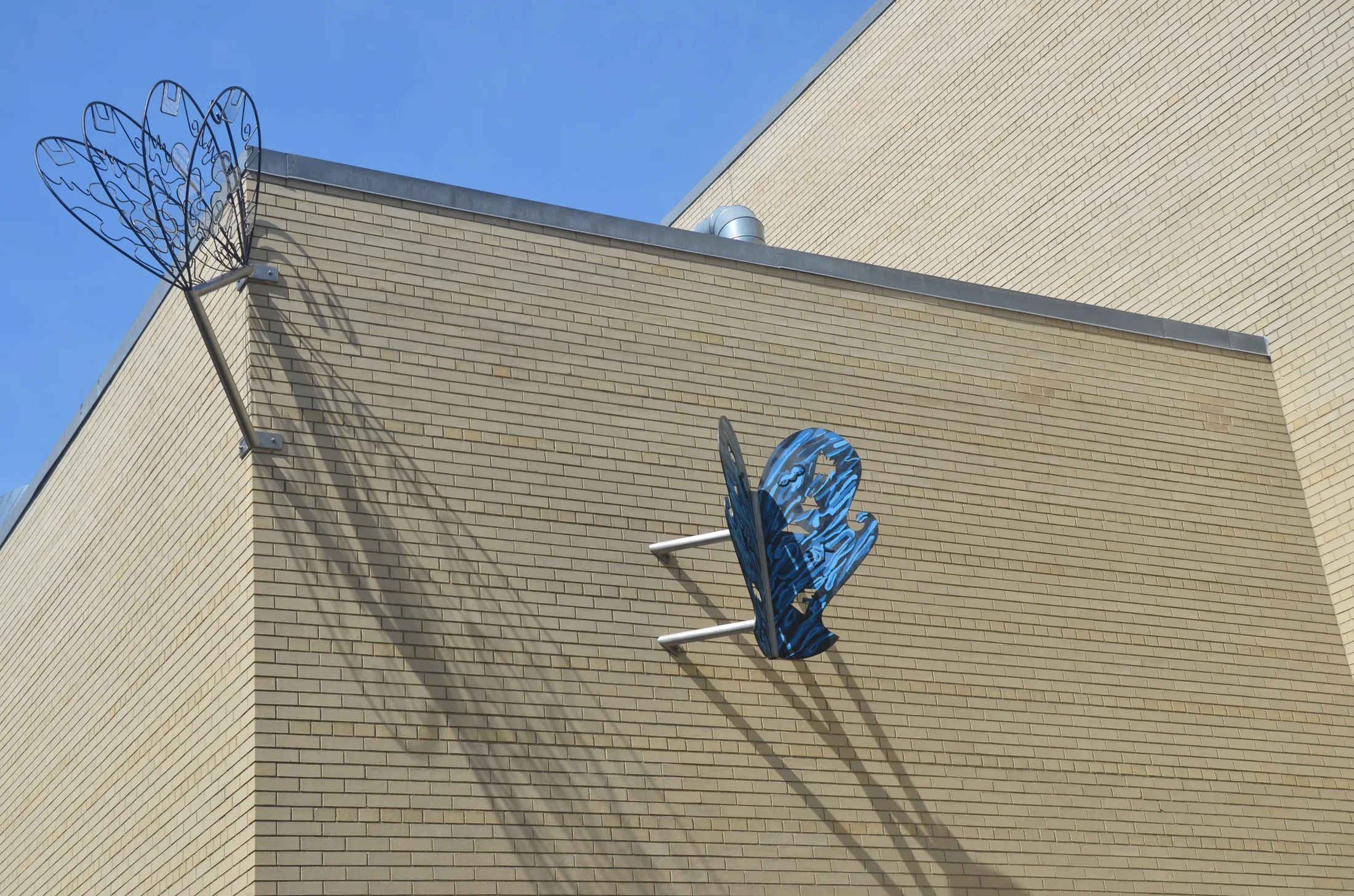 Two steel butterflies mounted to a tan colored brick building