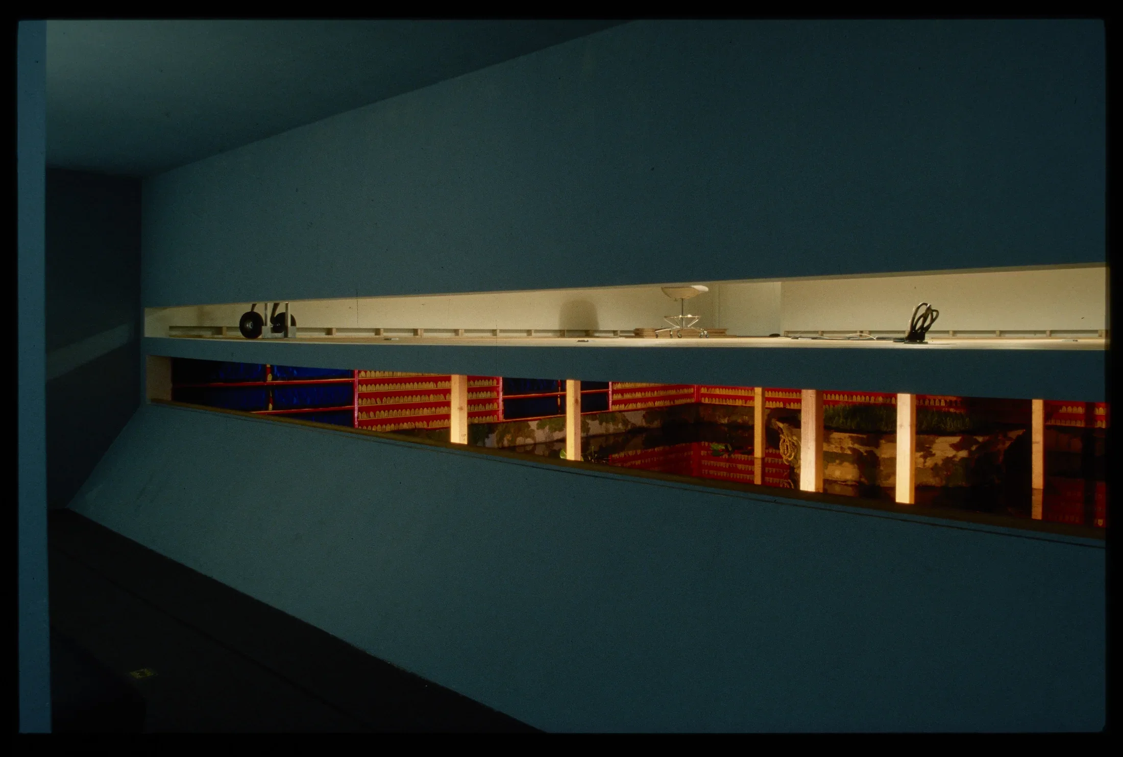 An island is surrounded by a pond within the gallery. The surrounding walls hold small tiles on red painted shelves.
