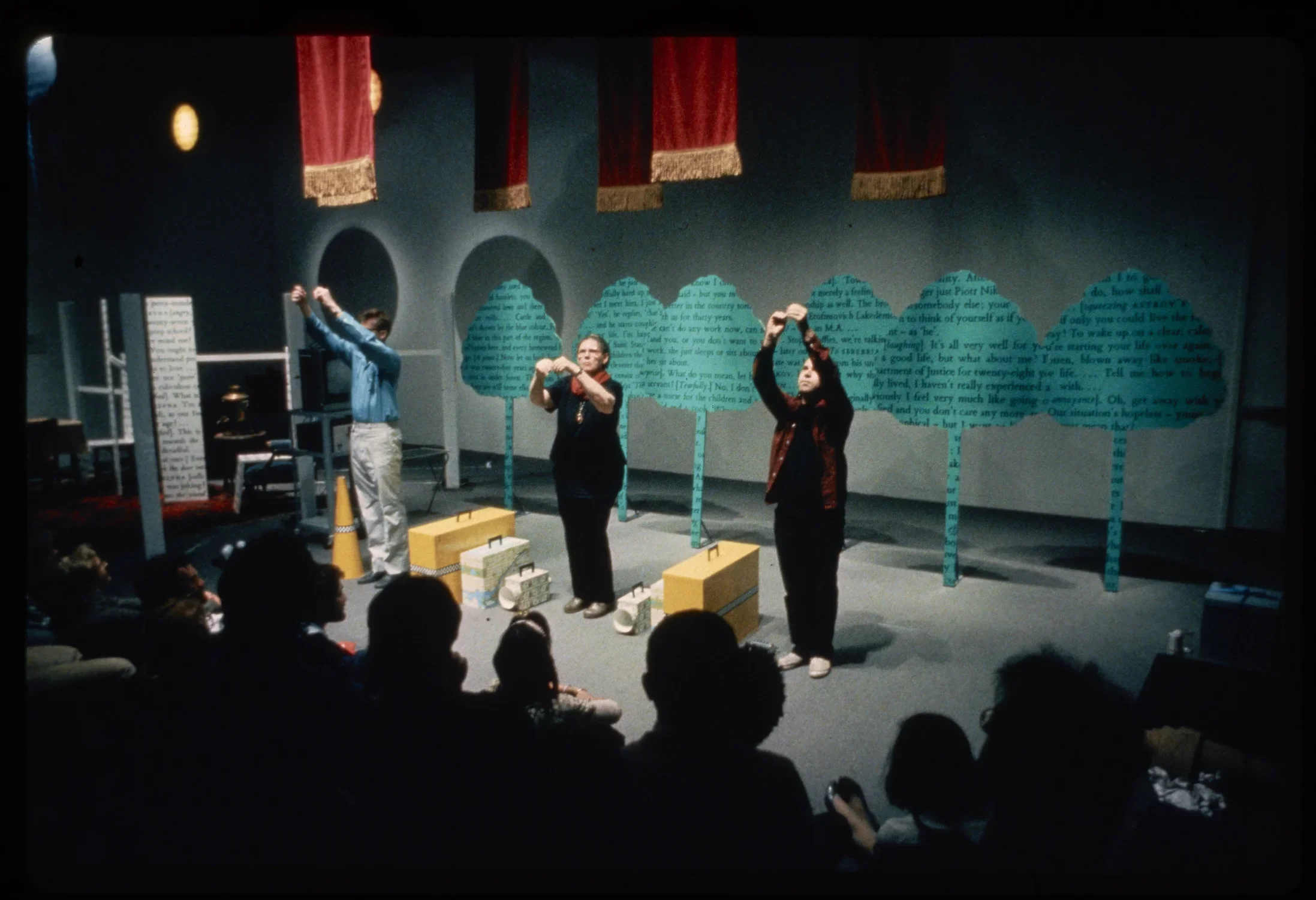 Three performers stand in front of the installation. With raised hands, they look up at a spotlight.