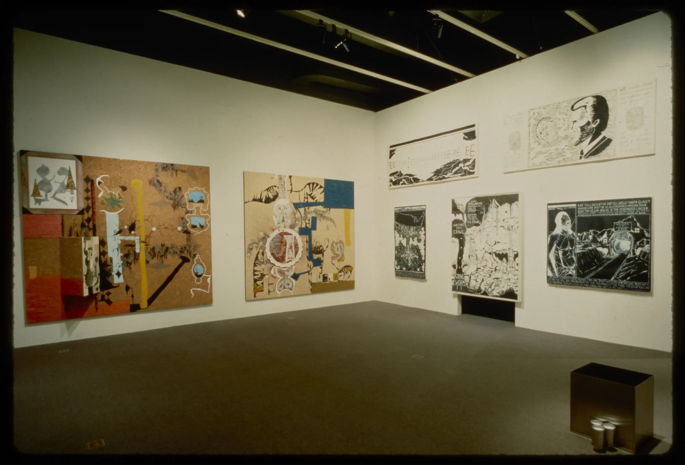 Two large wooden canvases with abstract colorful configurations are hung adjacent to five black and white comic style paintings.