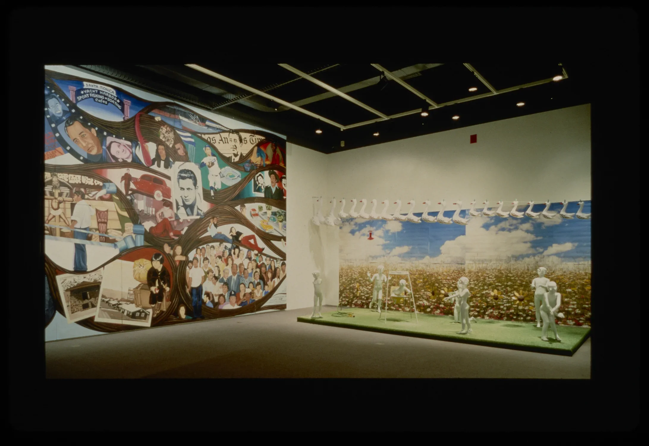 Wall mural of many people. Installation with white figures on faux grass in front of field background, under hanging geese.