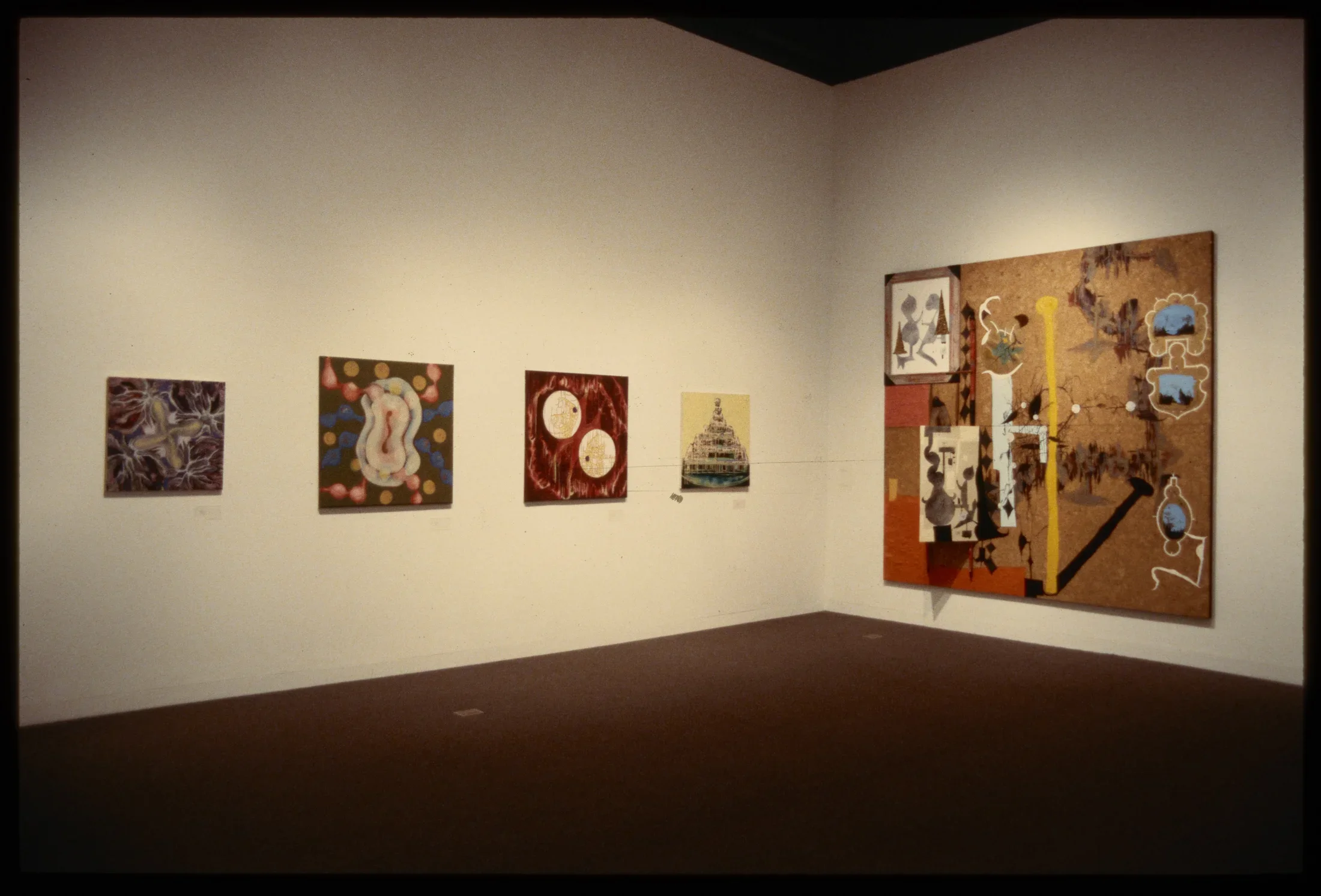 Four canvases with abstract colorful configurations are hung adjacent to large abstract colorful canvas.