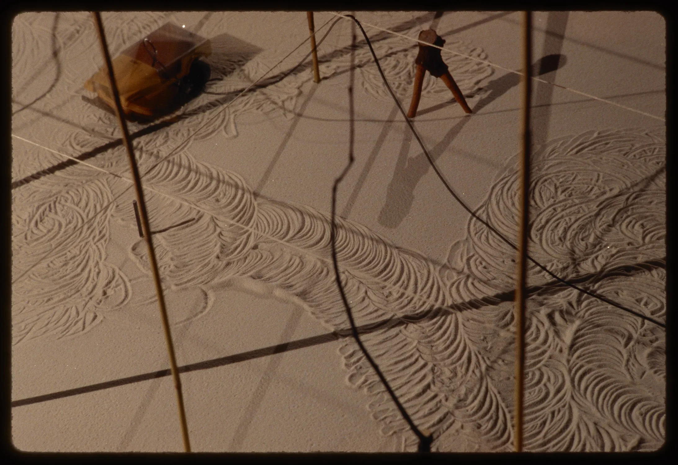 A small motorized car is shown in motion as it creates circular impressions in the surface of an installation. 
