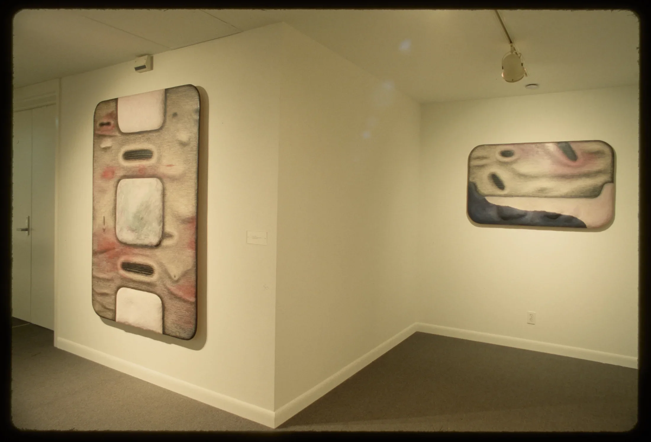 Two rectangular works with related abstract pink, grey, and black imagery hang on their own walls.