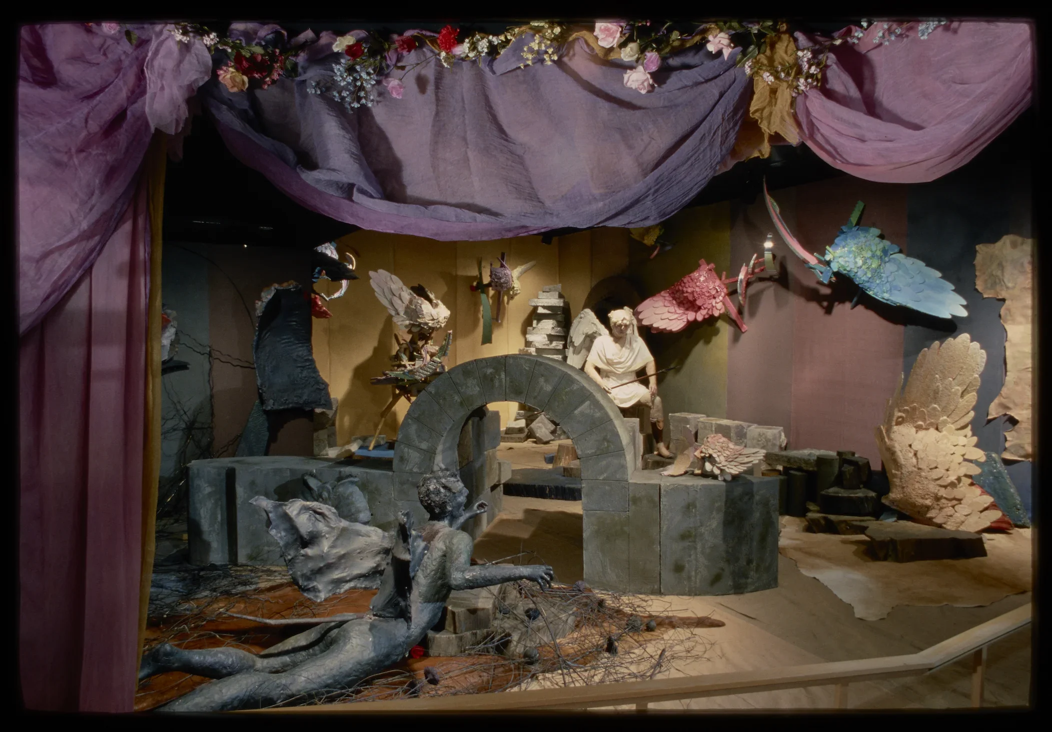 A large elaborate theatrical installation shows the archangel St. Michael, a sculpted archway, angel wings, purple curtains,  