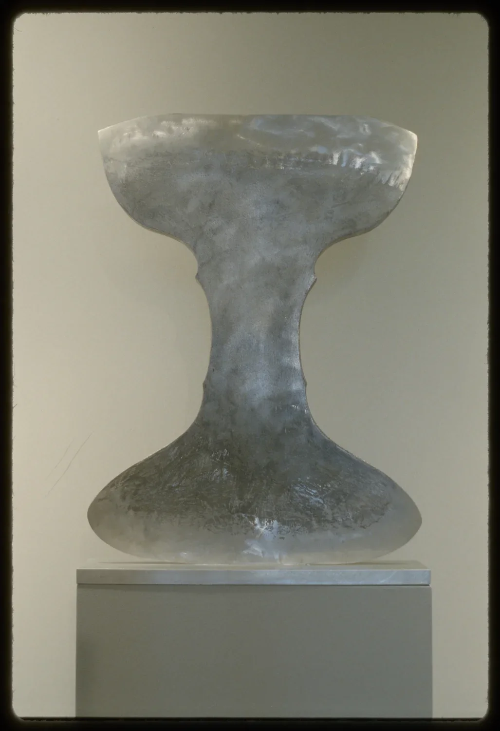 A metal sculpture in the shape of a cup or chalice of some kind. The light from the gallery reflects off of its surface. 