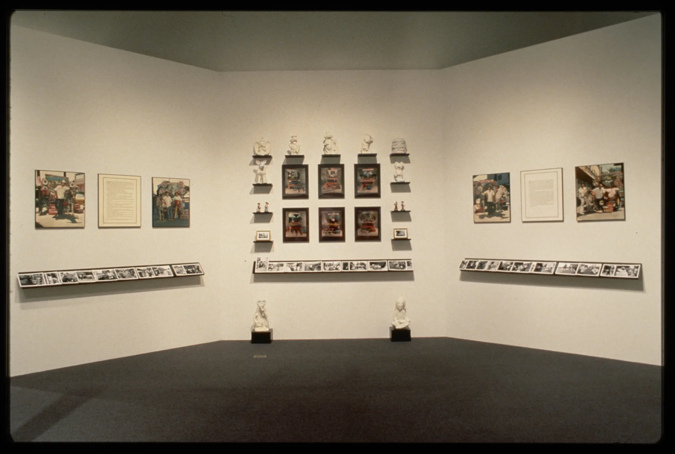 White sculptures line the wall in a square around colorful pictures. On either side colorful imagery hangs next to text. 
