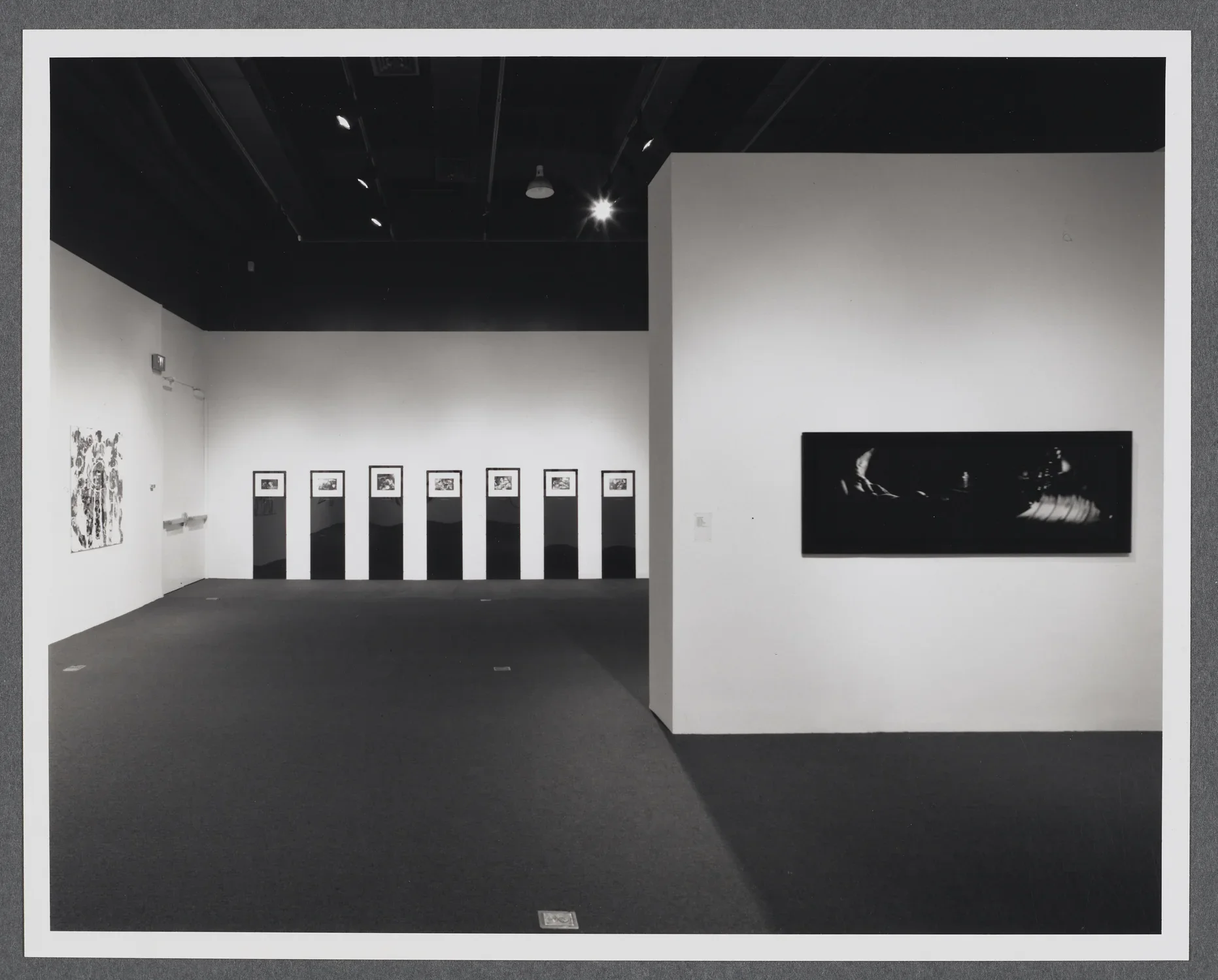 Large abstract artworks hang around the gallery space. A gallery wall stands in the center of the room.