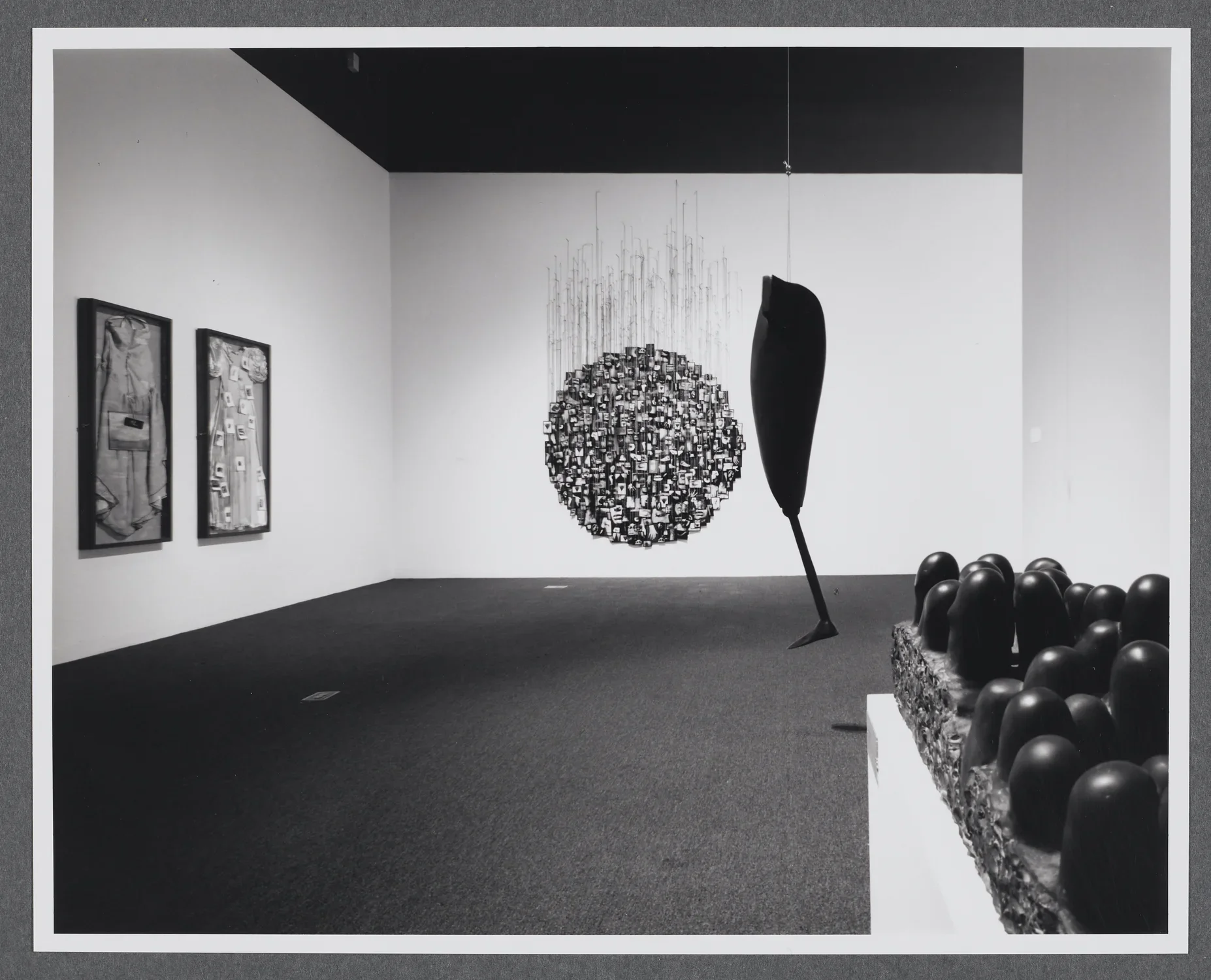 A sculpture of curved pillars emerging from a block sits in the foreground. A large black sculpture hangs in the background. 