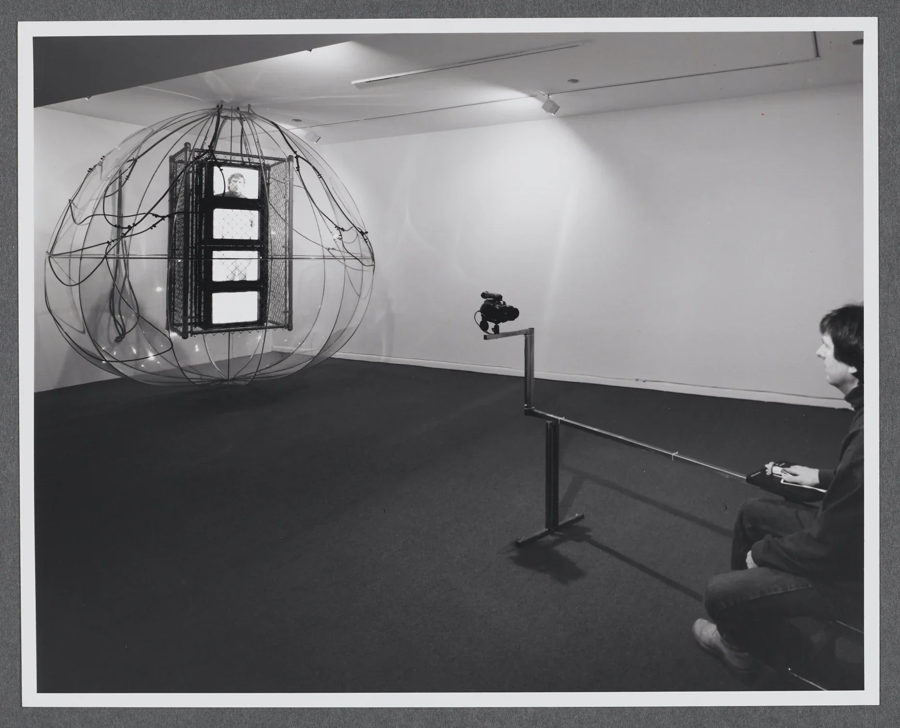A viewer sits in front of a camera as their image is then projected onto a monitor within the sculpture.