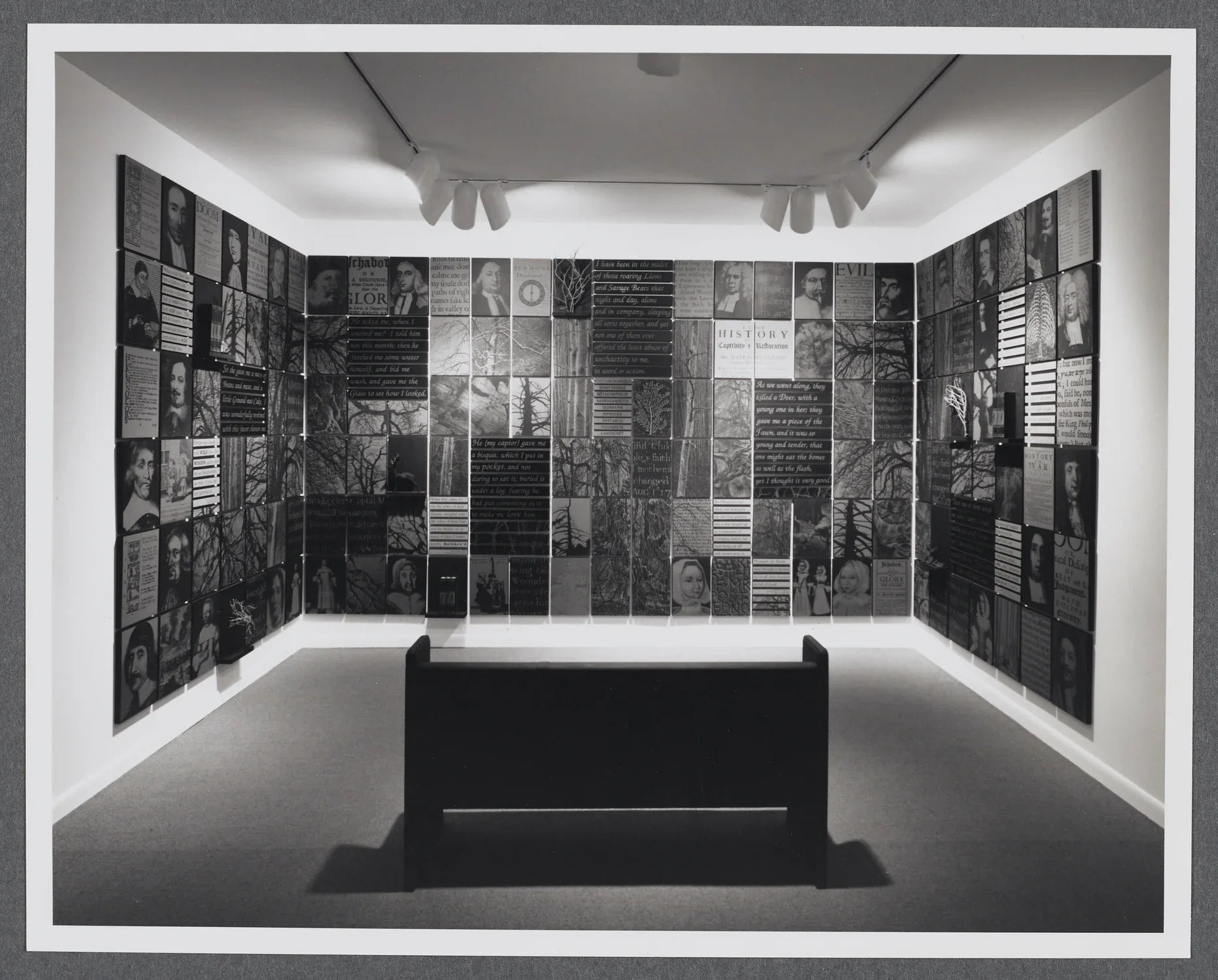 A bench sits in front of a gallery wall. On the wall are photos of historical portraits as well as historical documents.  