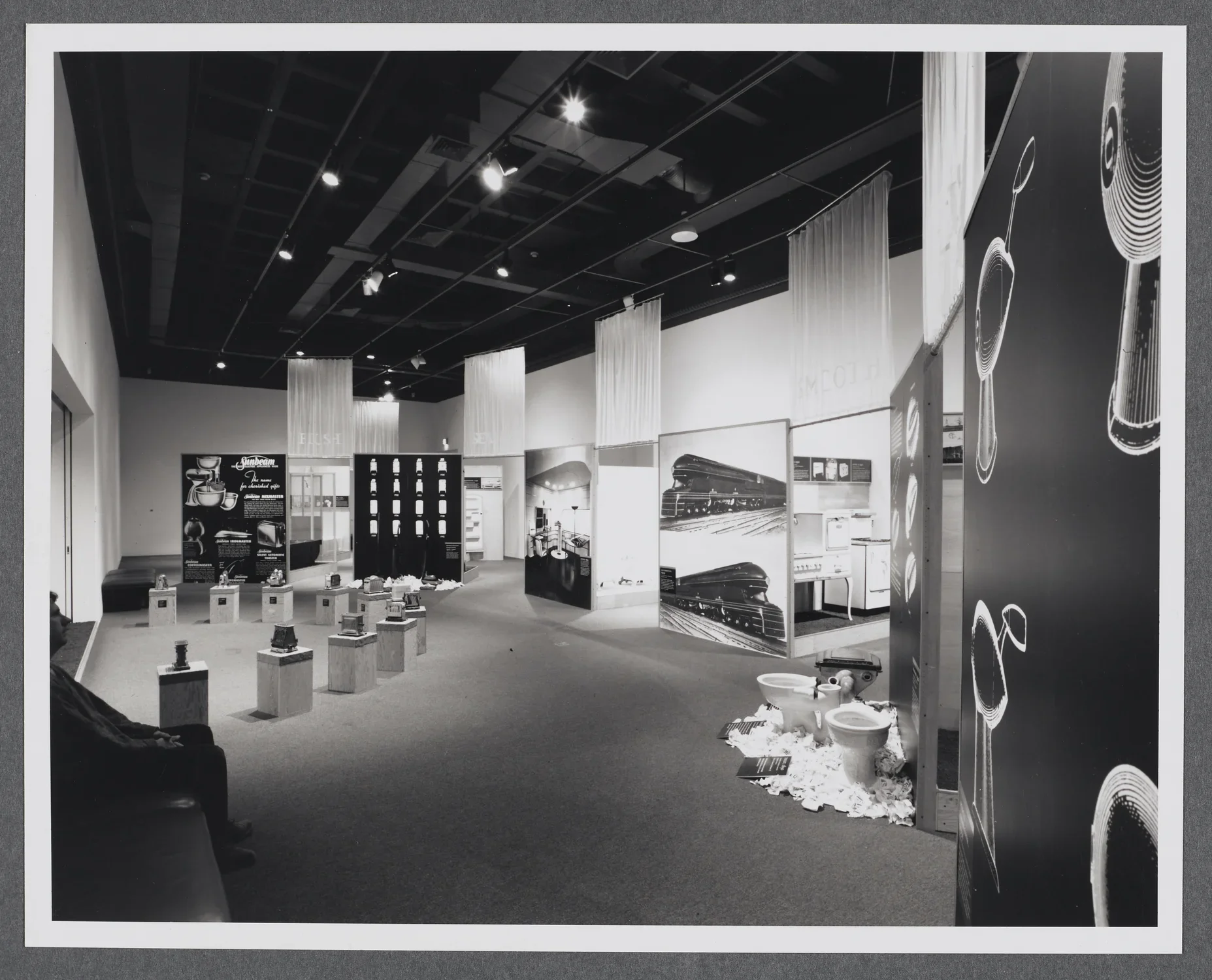 An installation view of the gallery where large diagrams and images are paired with household items they describe. 