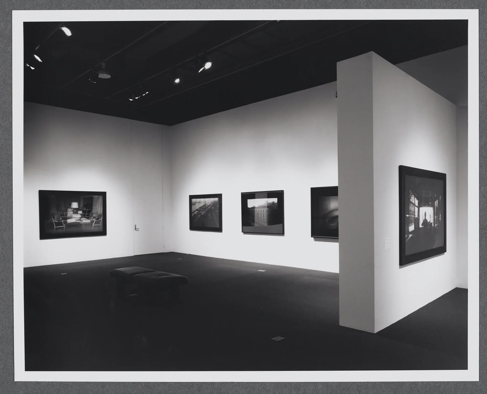 Photographs of different sizes line the gallery walls. A bench is in the center of the gallery for viewing the works.