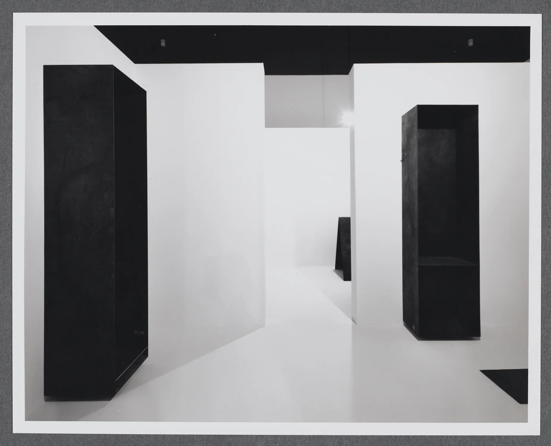 Large steel rectangular sculptures stand contrasted against white walls. Other geometric forms stand in the next space.